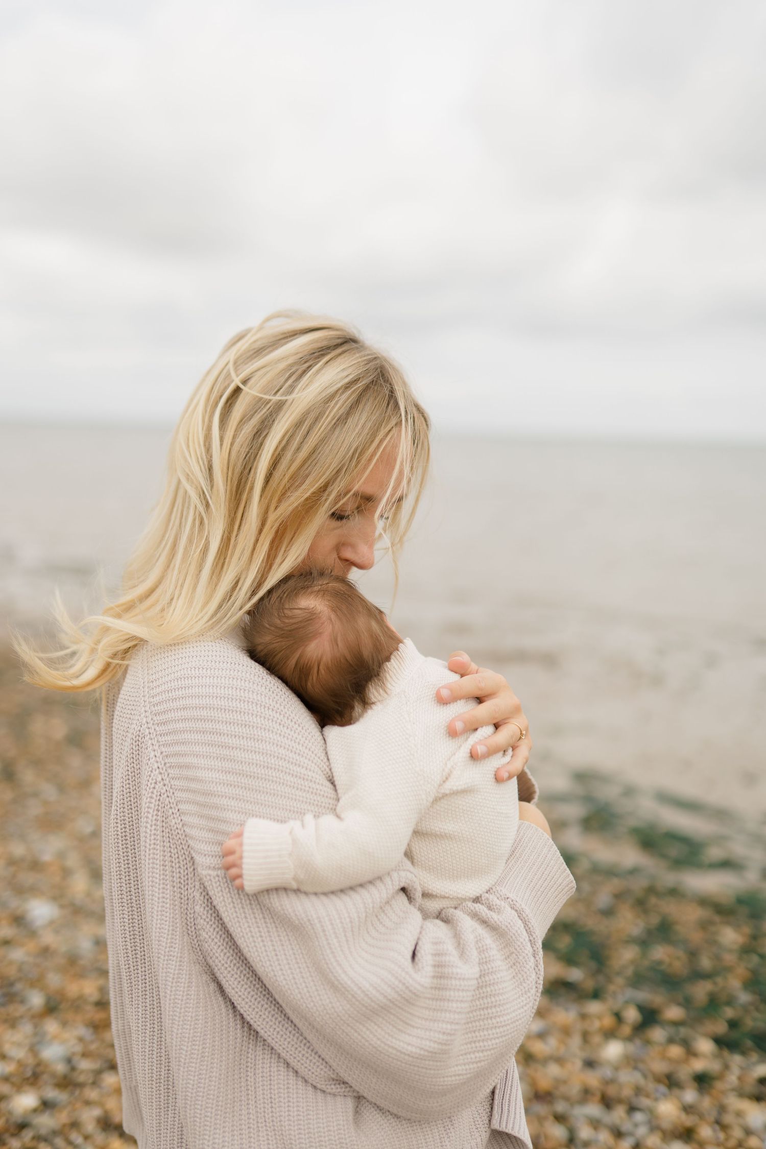 A tender moment captured on a cloudy beach day in soft, muted tones.