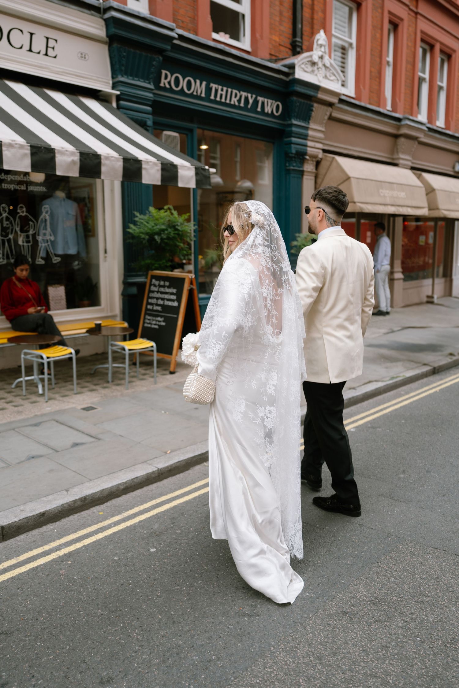 A couple in wedding attire walks past Room Thirty Two and Monocle storefronts.