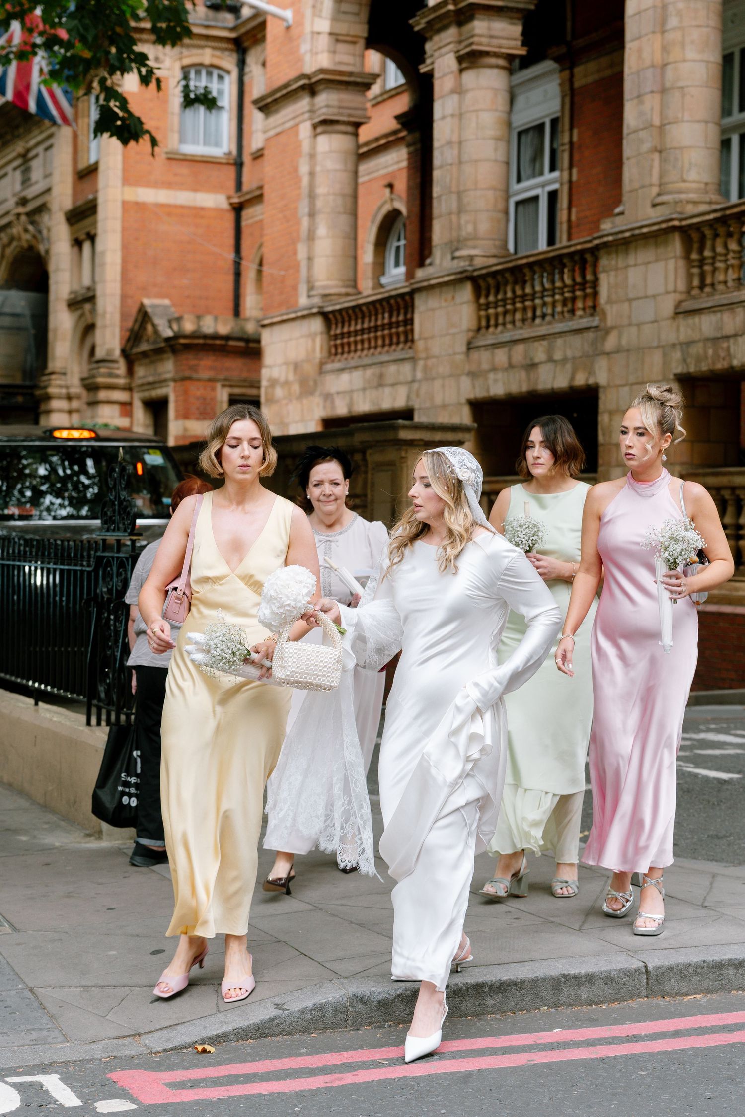Wedding party running down city street in pastel dresses.