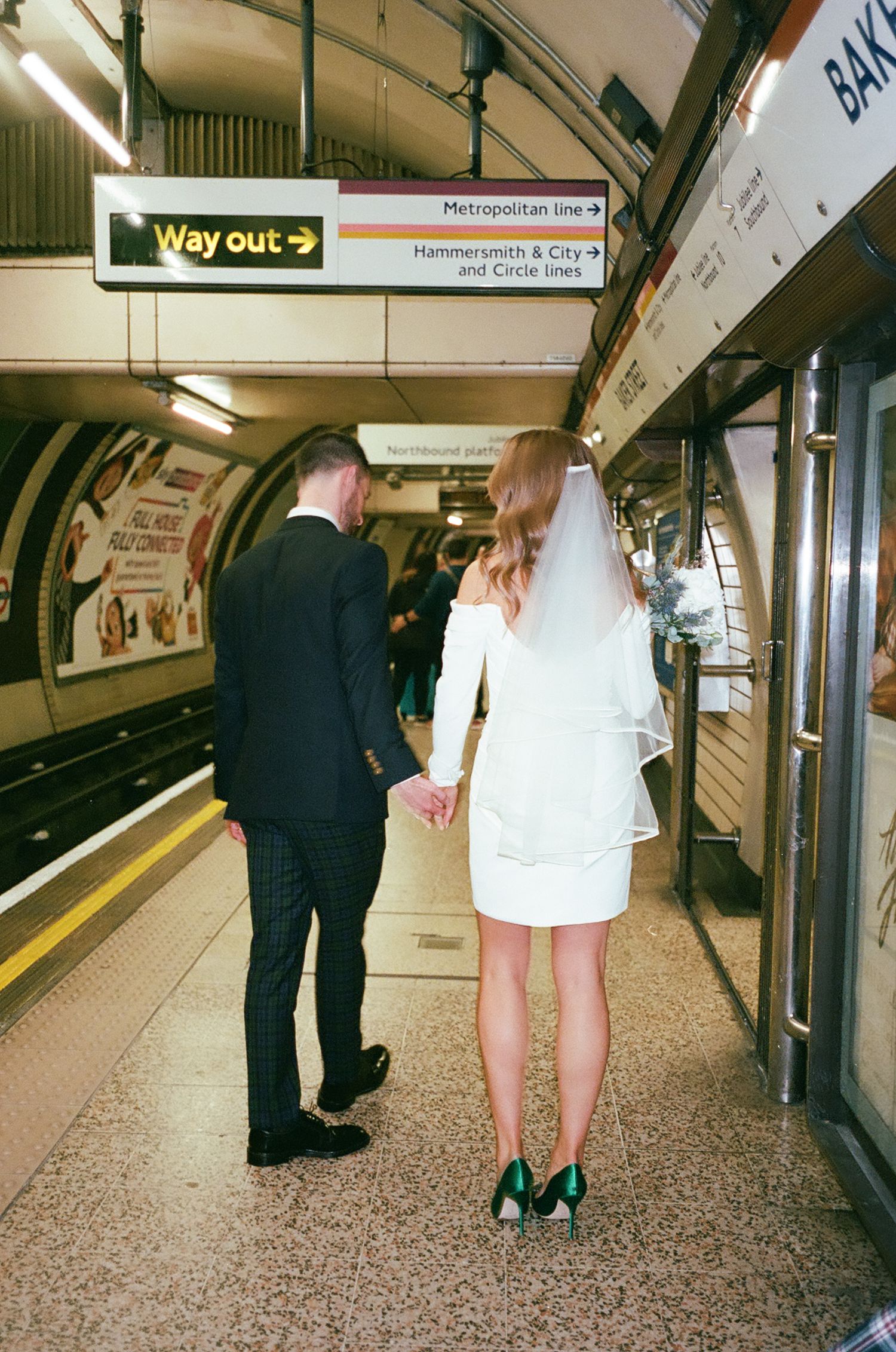 Two people in formal attire walk through a London Underground station platform.