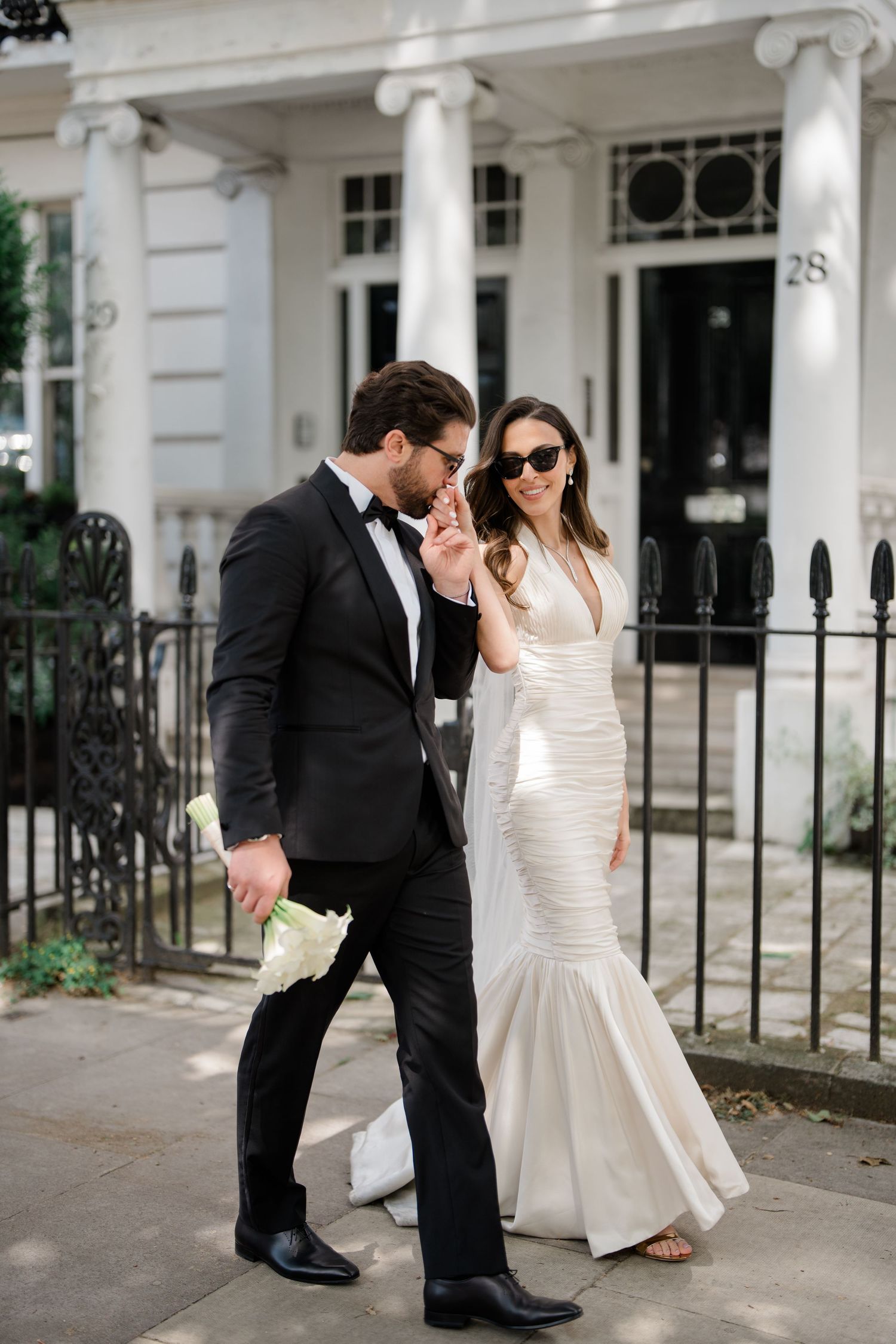 A couple in formal attire poses together on a white stone staircase outside an elegant building in London.