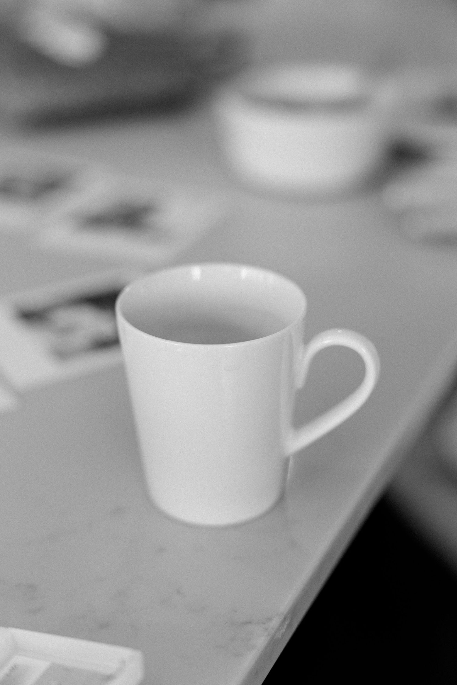 Minimalist black and white photo of white coffee cup on plain surface.