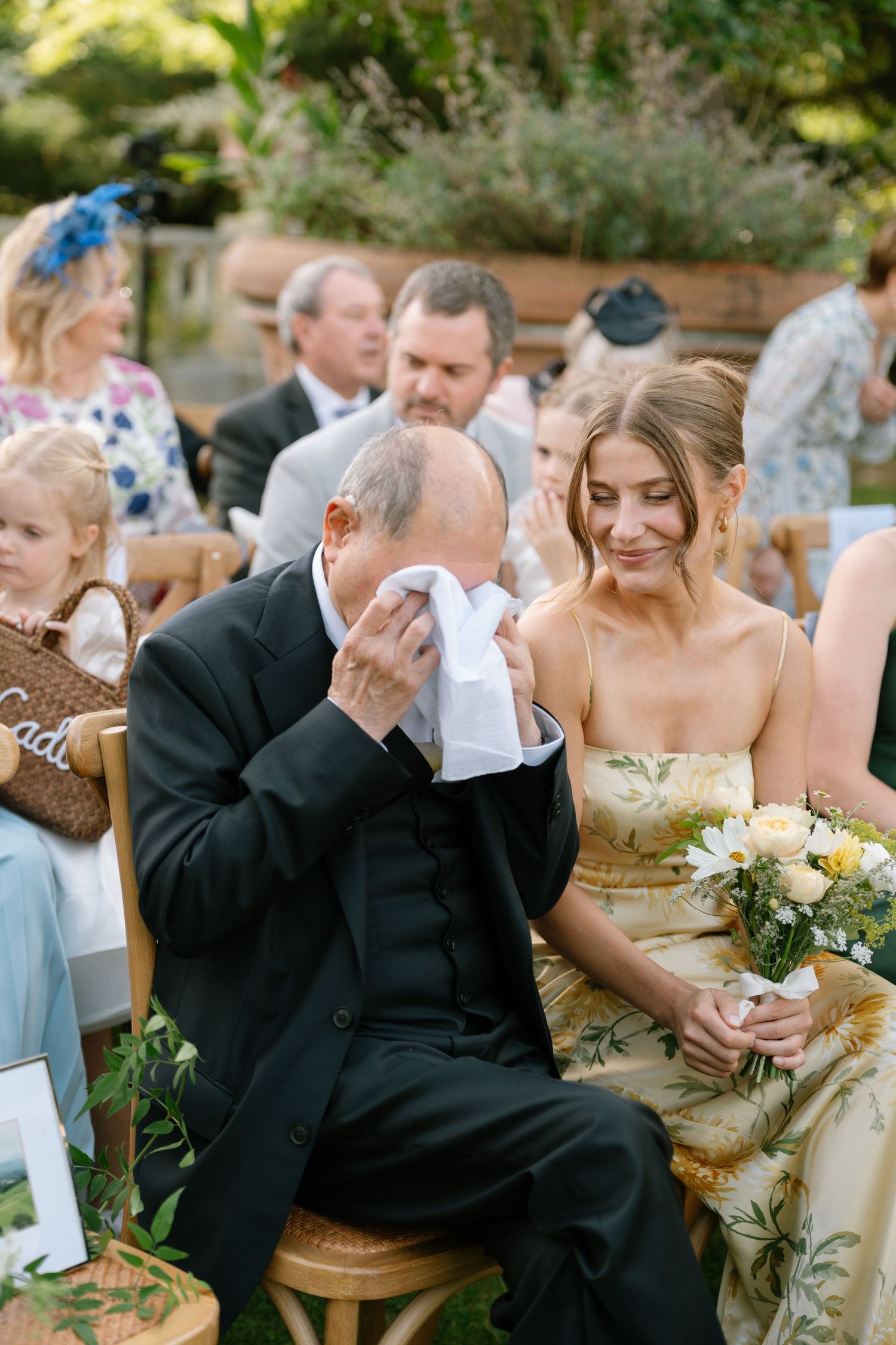 Emotional wedding guests wipe away tears during an outdoor garden ceremony.