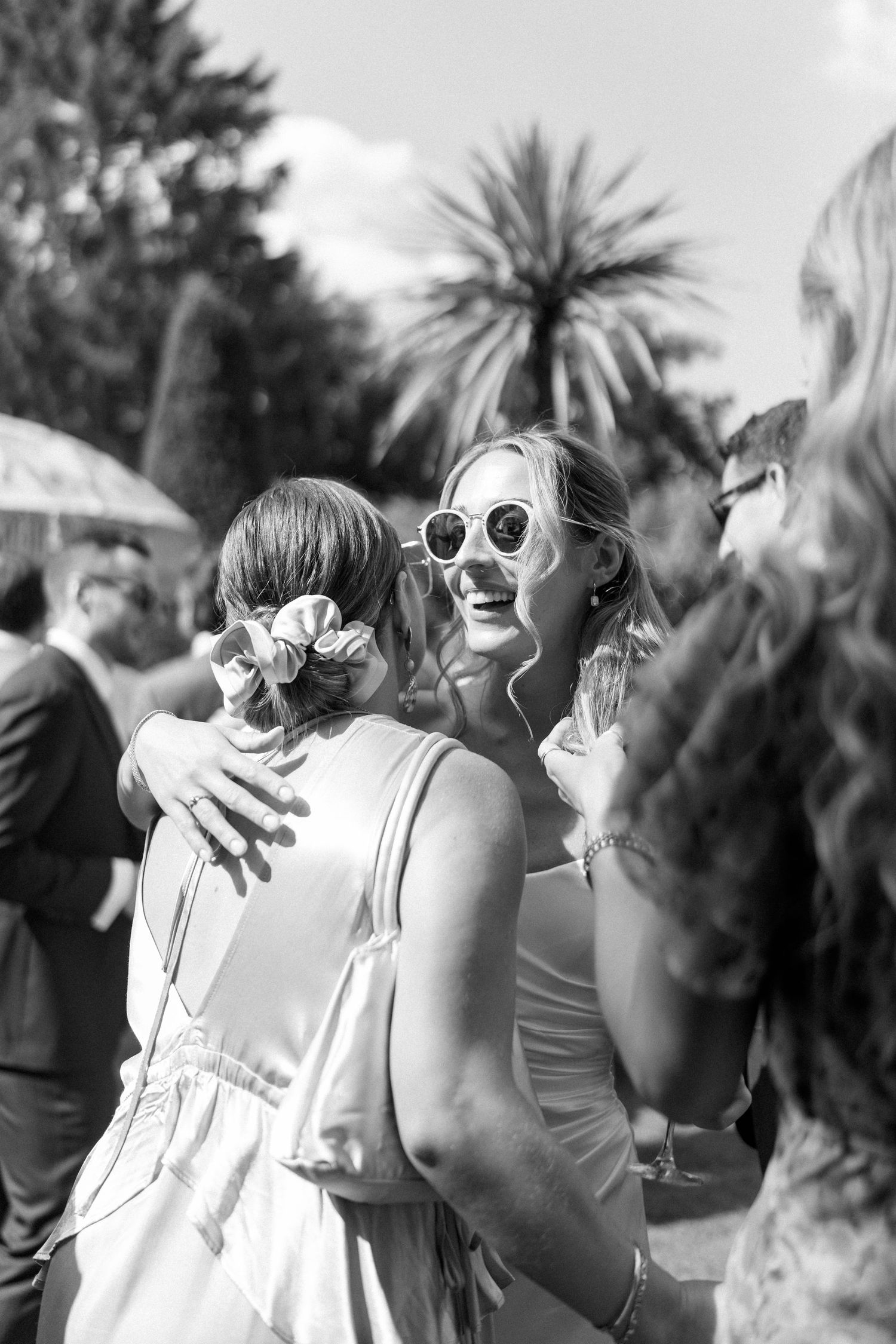 Wedding guests in sunglasses celebrating outdoors with palm trees in background.