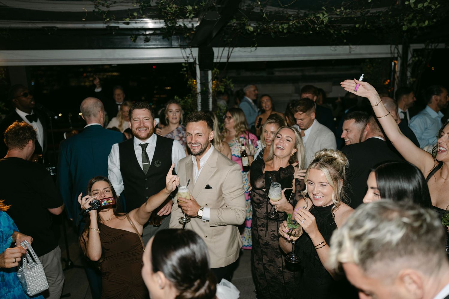 Wedding reception guests dancing and celebrating on a dark dance floor.