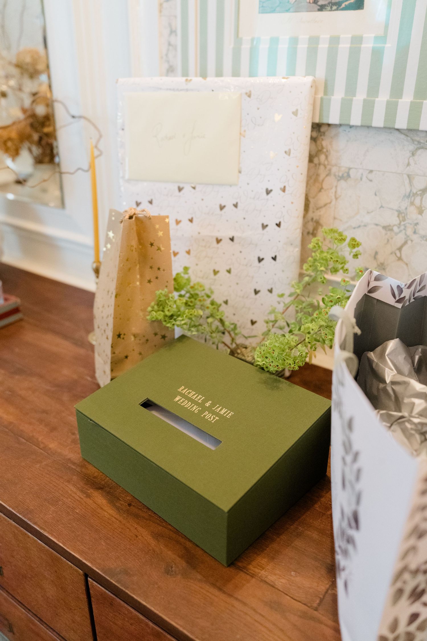 Green wedding card box labeled Rachael & Jamie on a wooden dresser with gifts and floral decorations.
