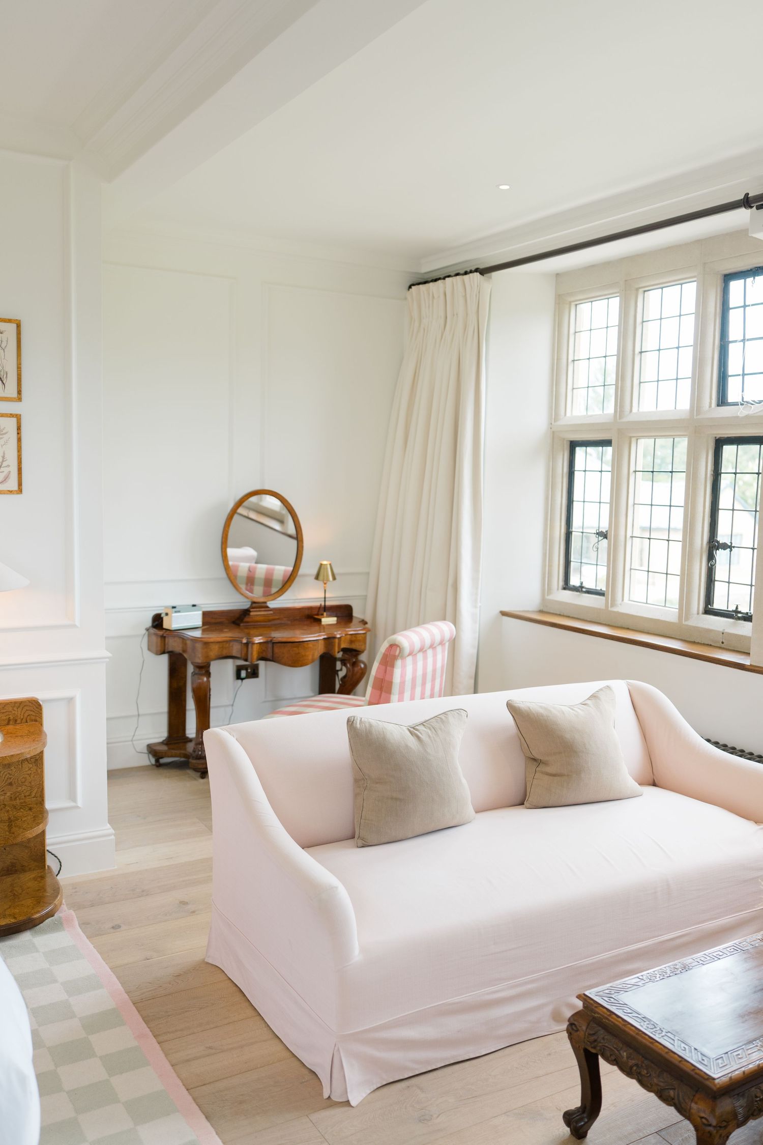 Elegant bright bridal suite with pink sofa, vintage dressing table, leaded windows and neutral decor.