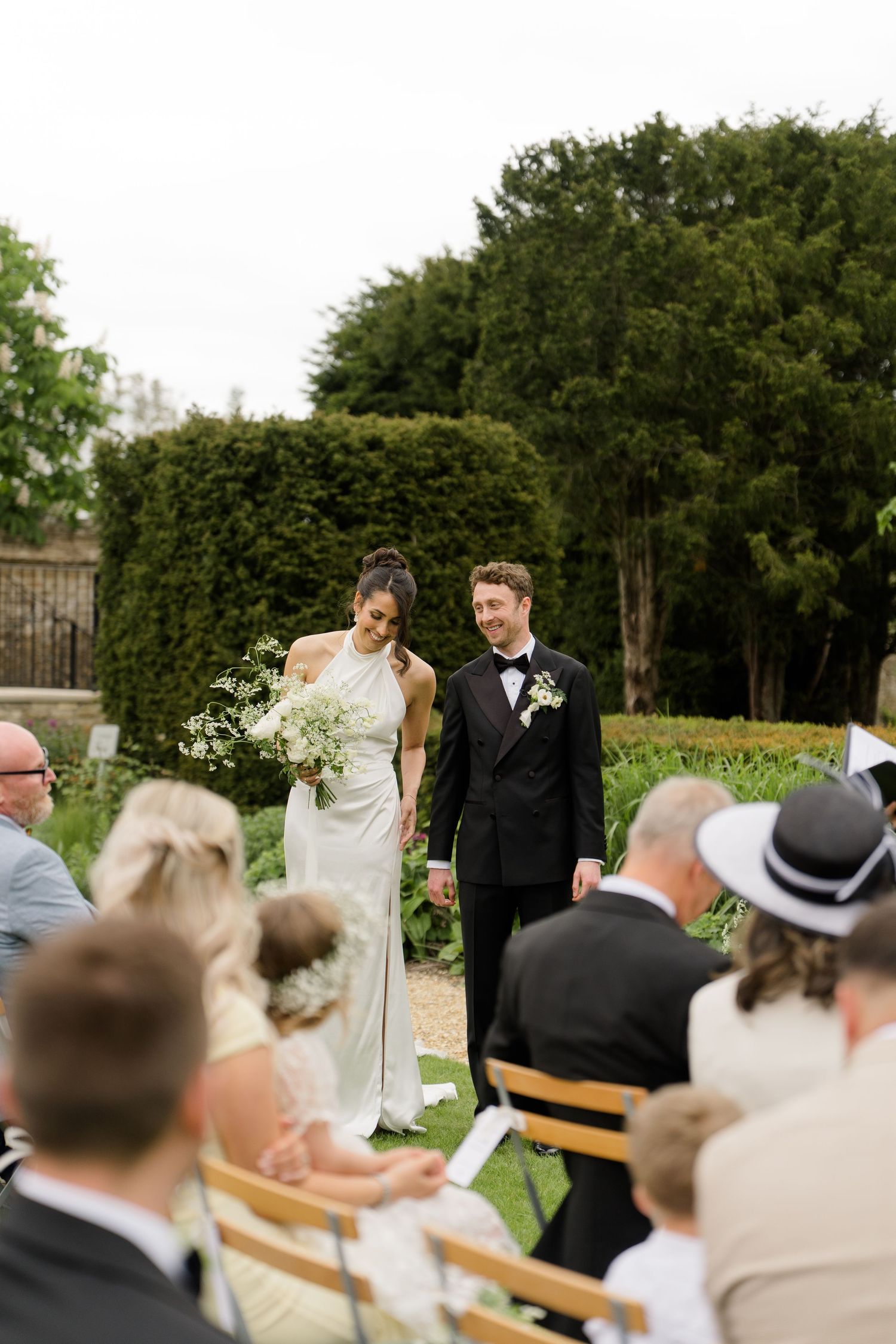 Bride and groom walking down outdoor aisle at garden wedding ceremony holding bouquet.