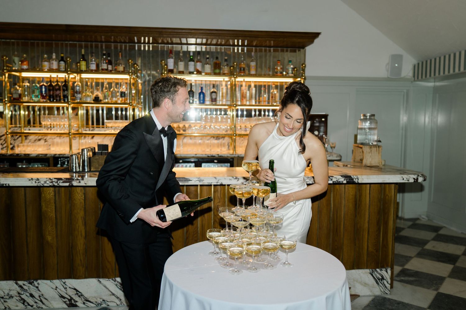 Bride and groom pouring champagne tower at elegant bar during wedding reception.