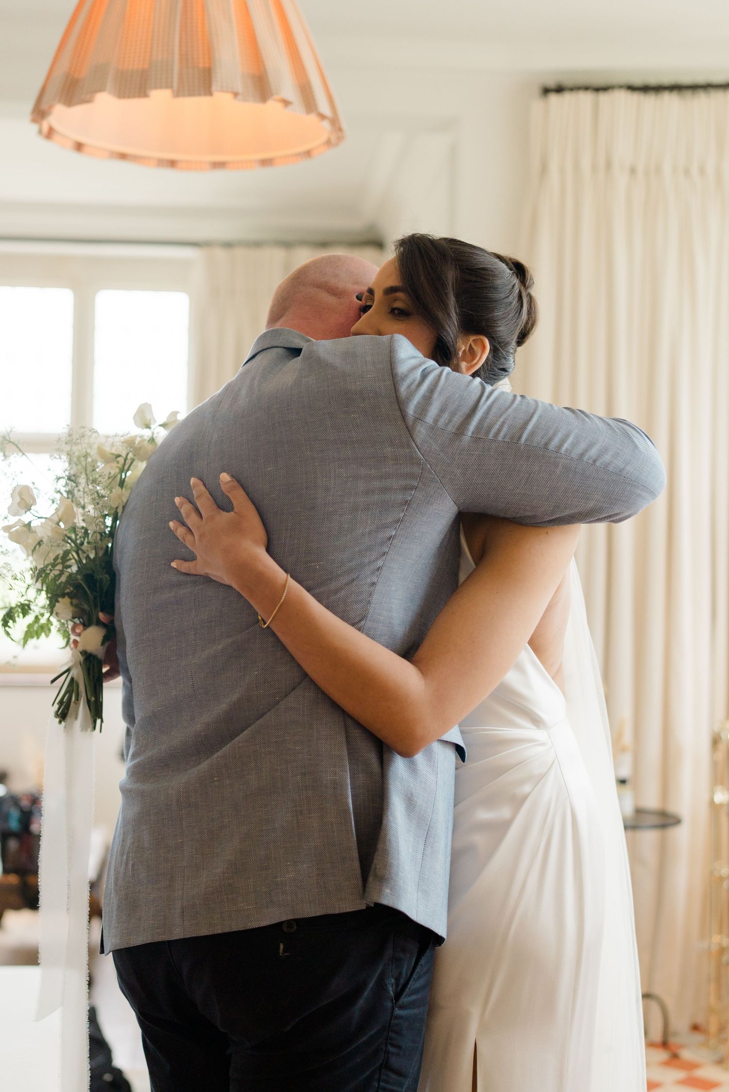 Bride in white gown shares emotional hug with father before wedding ceremony.