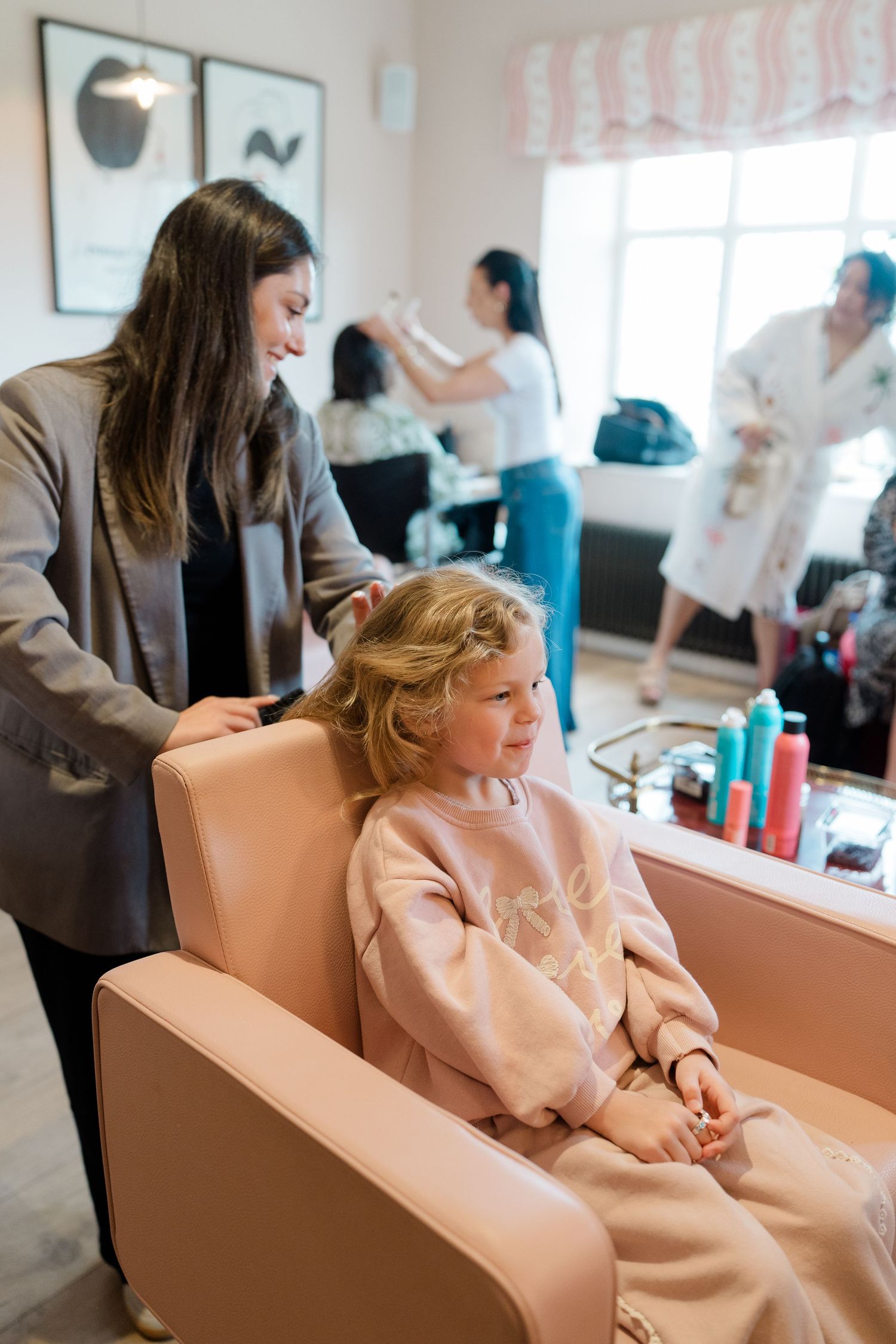 Hair stylist styling a young blonde girls hair in a pink salon chair during bridal wedding preparations.