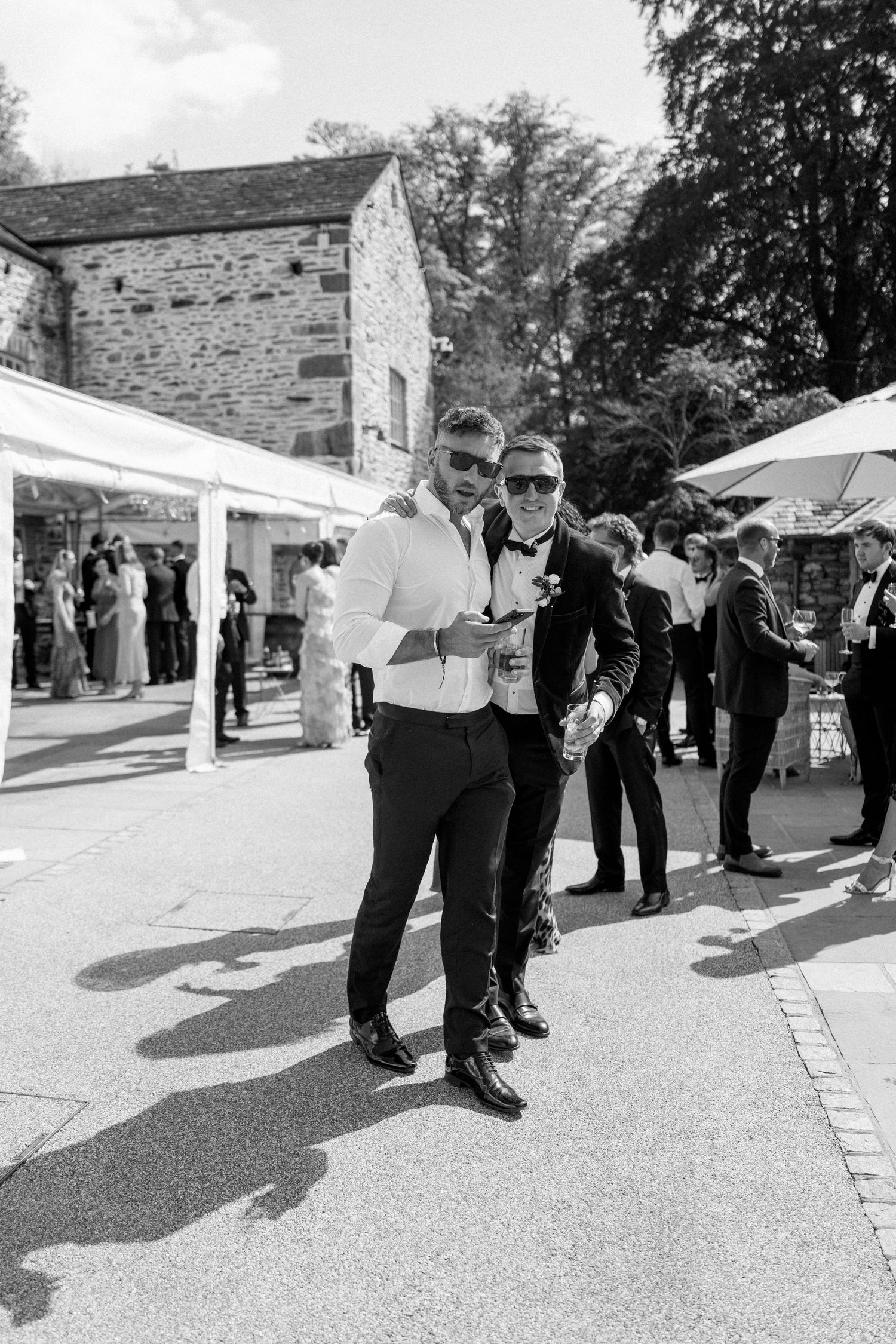 Black and white photo of wedding guests mingling outside a stone venue.