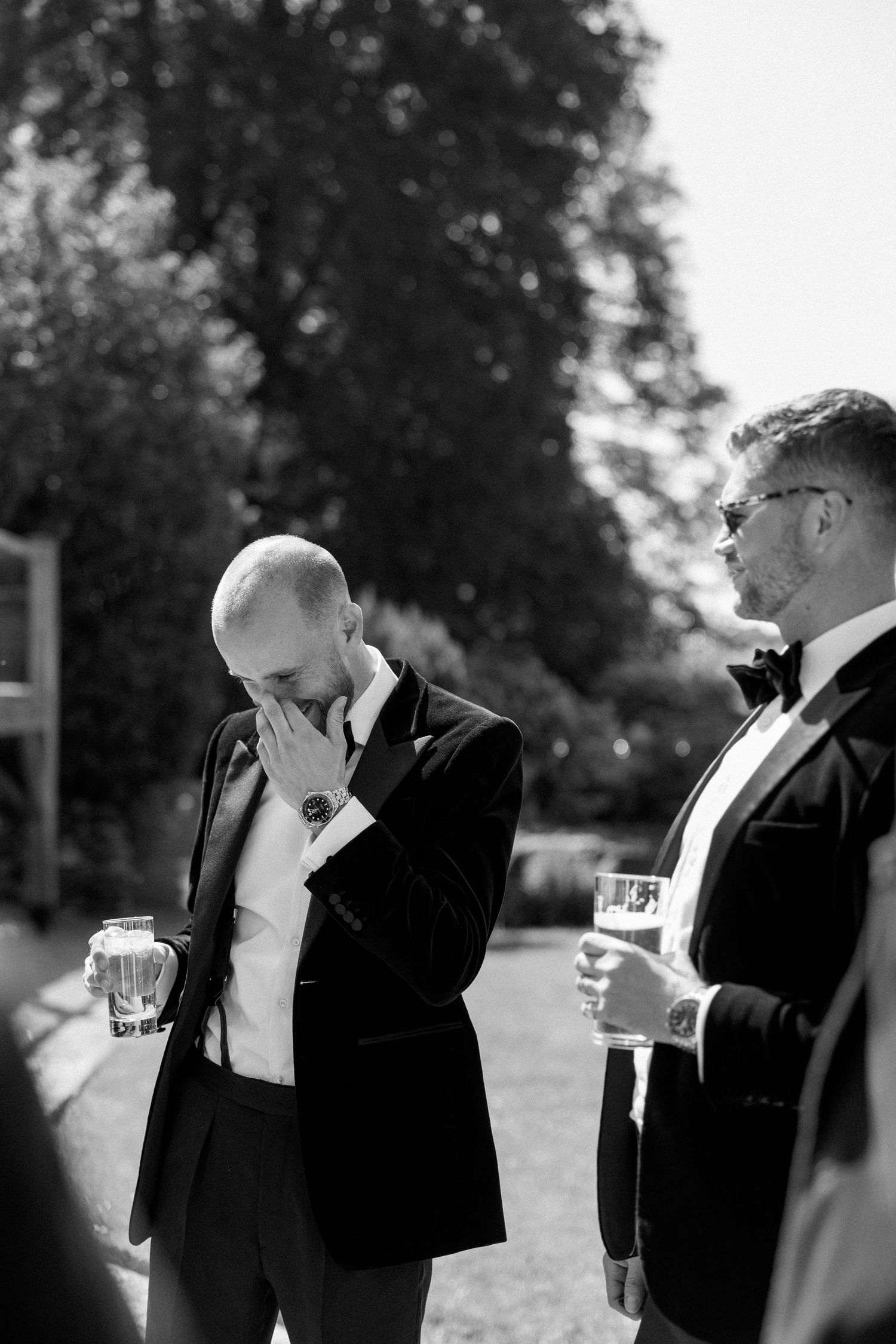Black and white photo of men in formal wear having drinks outdoors.