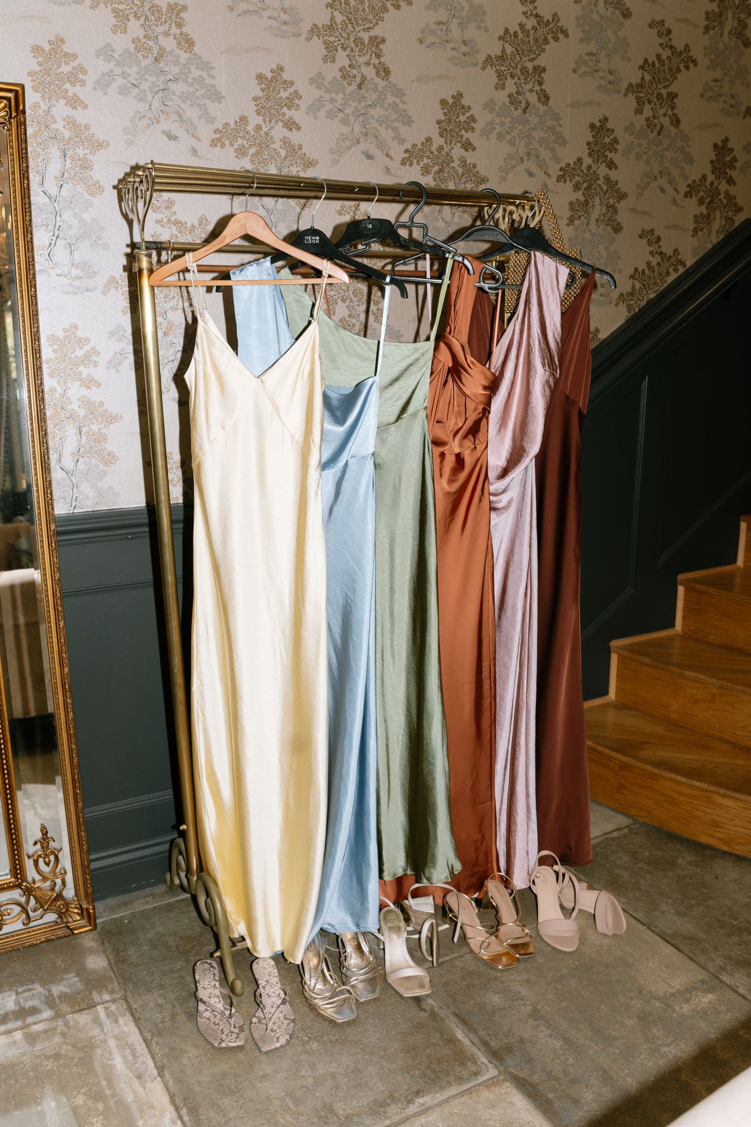 Row of pastel colored bridesmaid dresses hanging on display with elegant shoes beneath.