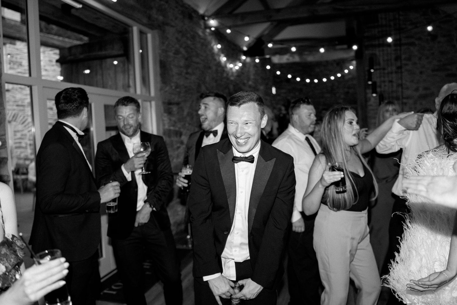 Formal event guests mingling and dancing under string lights in a rustic stone venue.