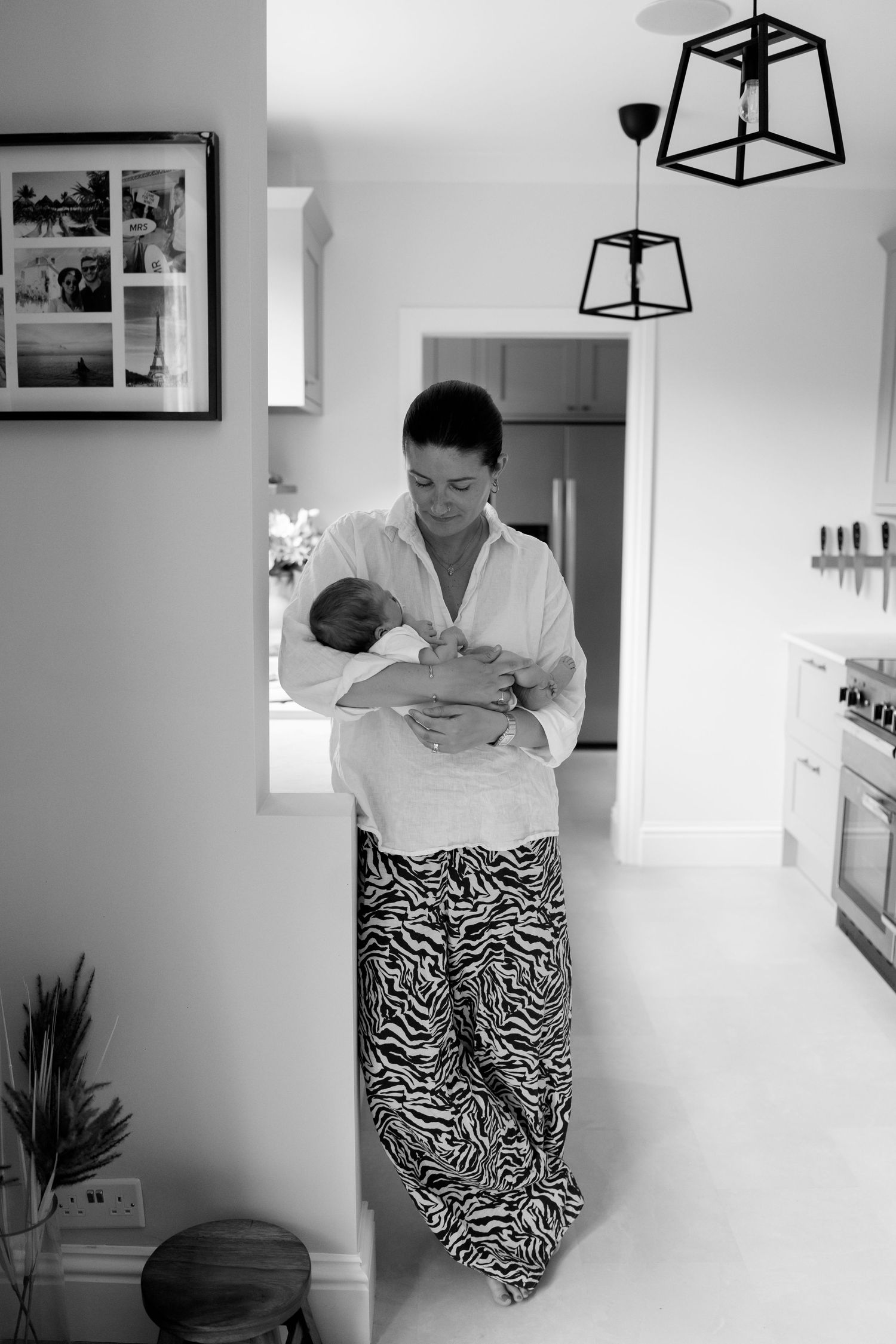 Black and white photos of parent holding baby in modern white kitchen interior.