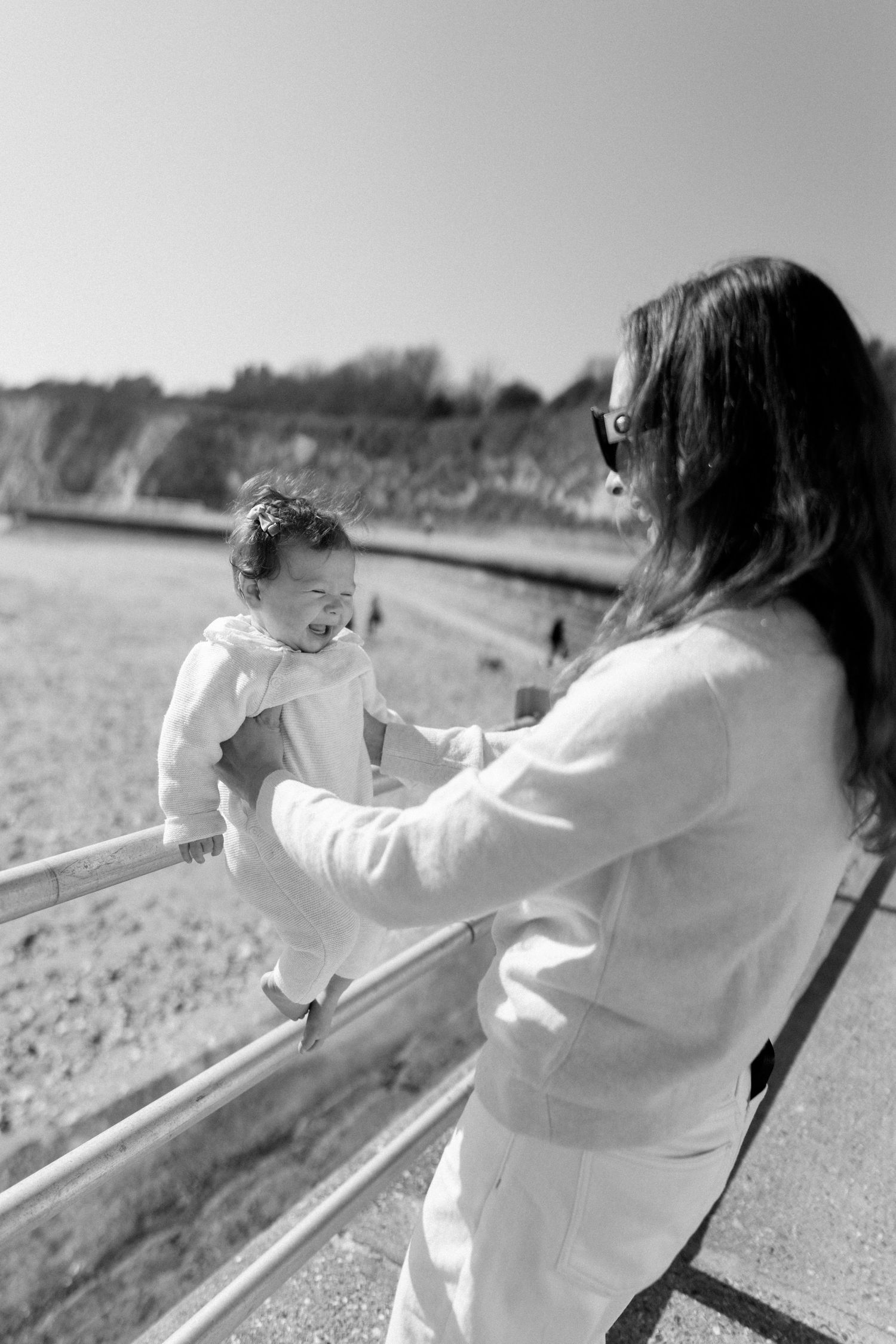 Parent and baby in matching white outfits playing together on a railing outdoors.