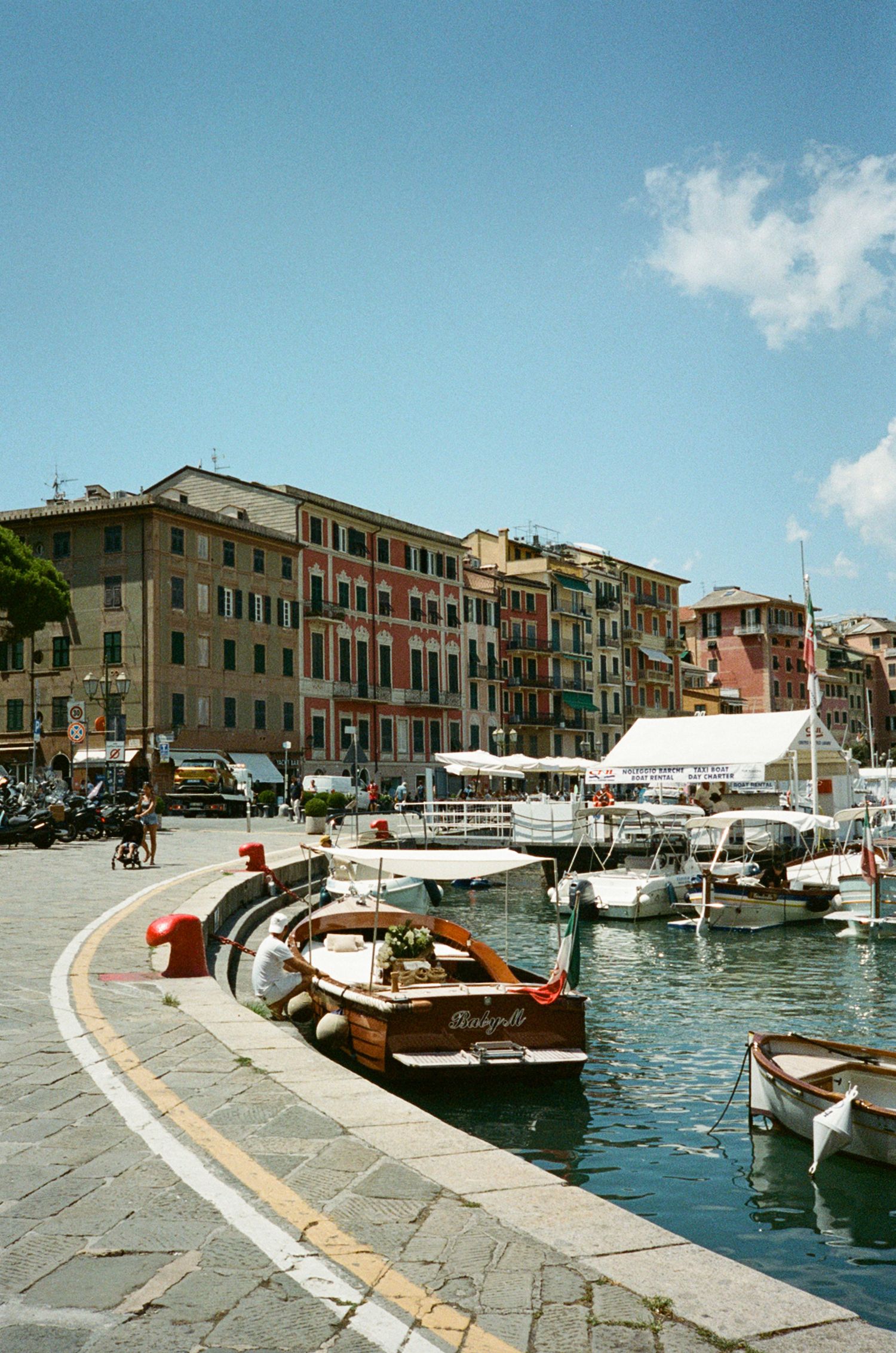 Colorful Italian harbor with moored boats, waterfront buildings, and clear blue sky on sunny day.