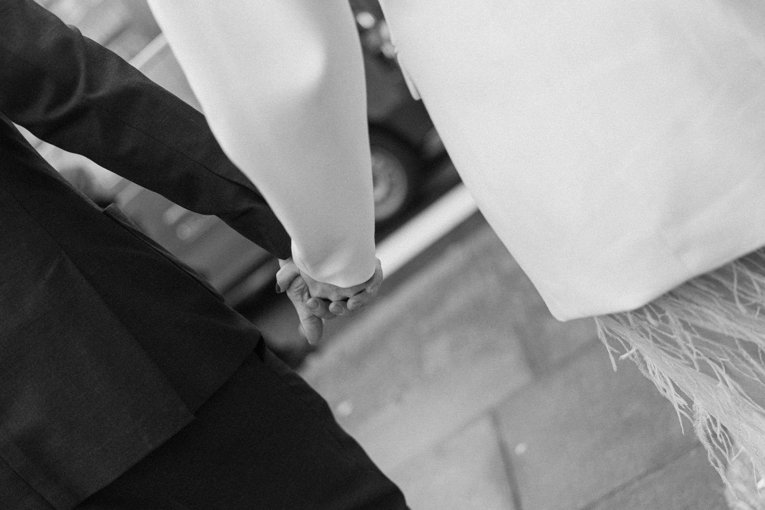Black and white close-up of bride and groom holding hands on wedding day.