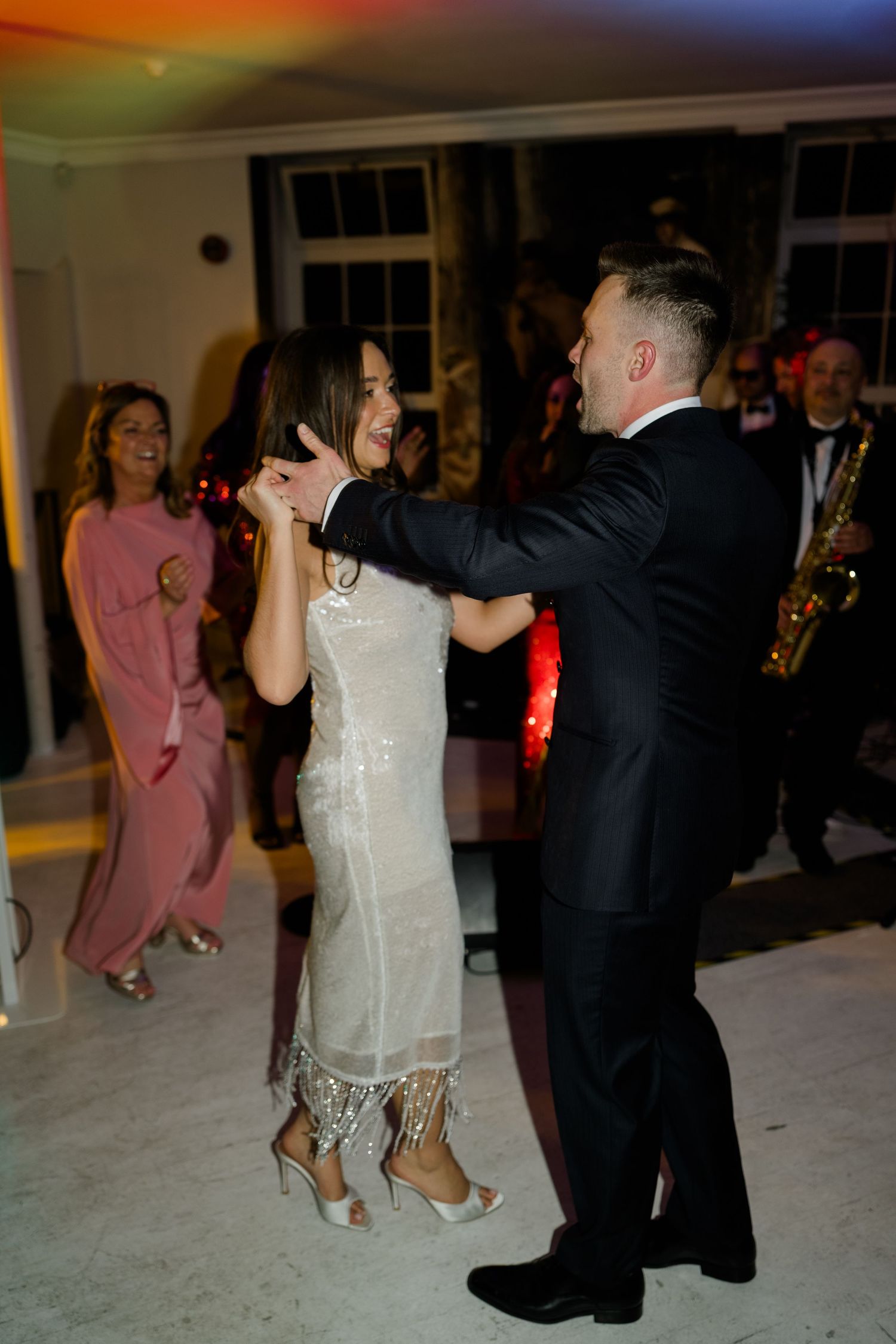 Bride and groom share their first dance surrounded by guests and a live saxophonist.