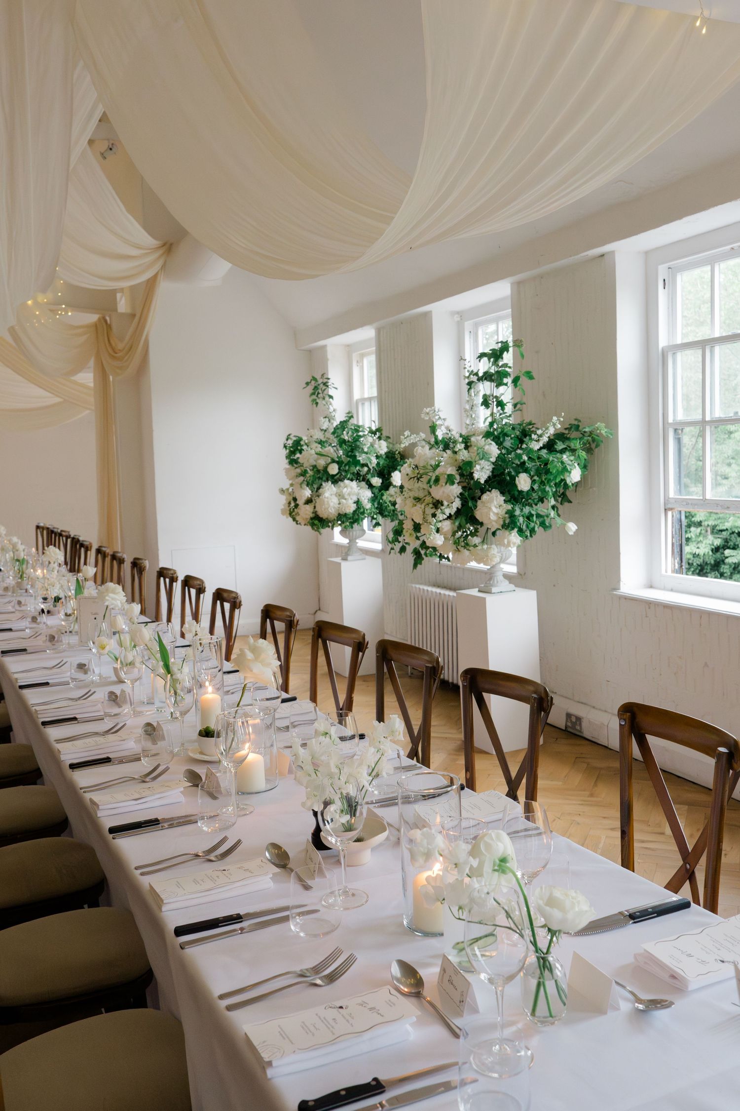 Elegant wedding reception hall with long white tables, candles, and tall floral centerpieces.
