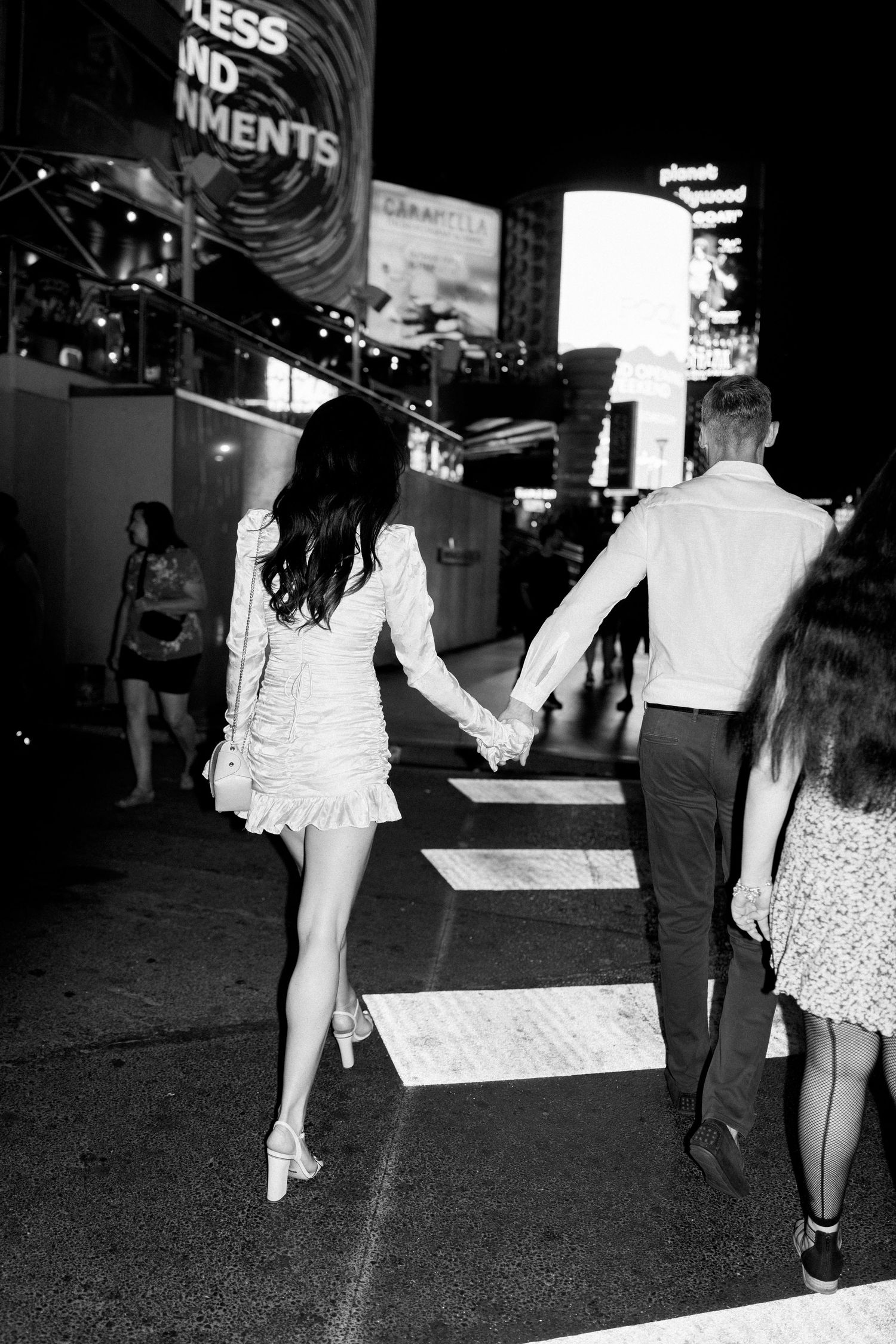 A black and white nighttime photo of a couple walking through Las Vegas holding hands.