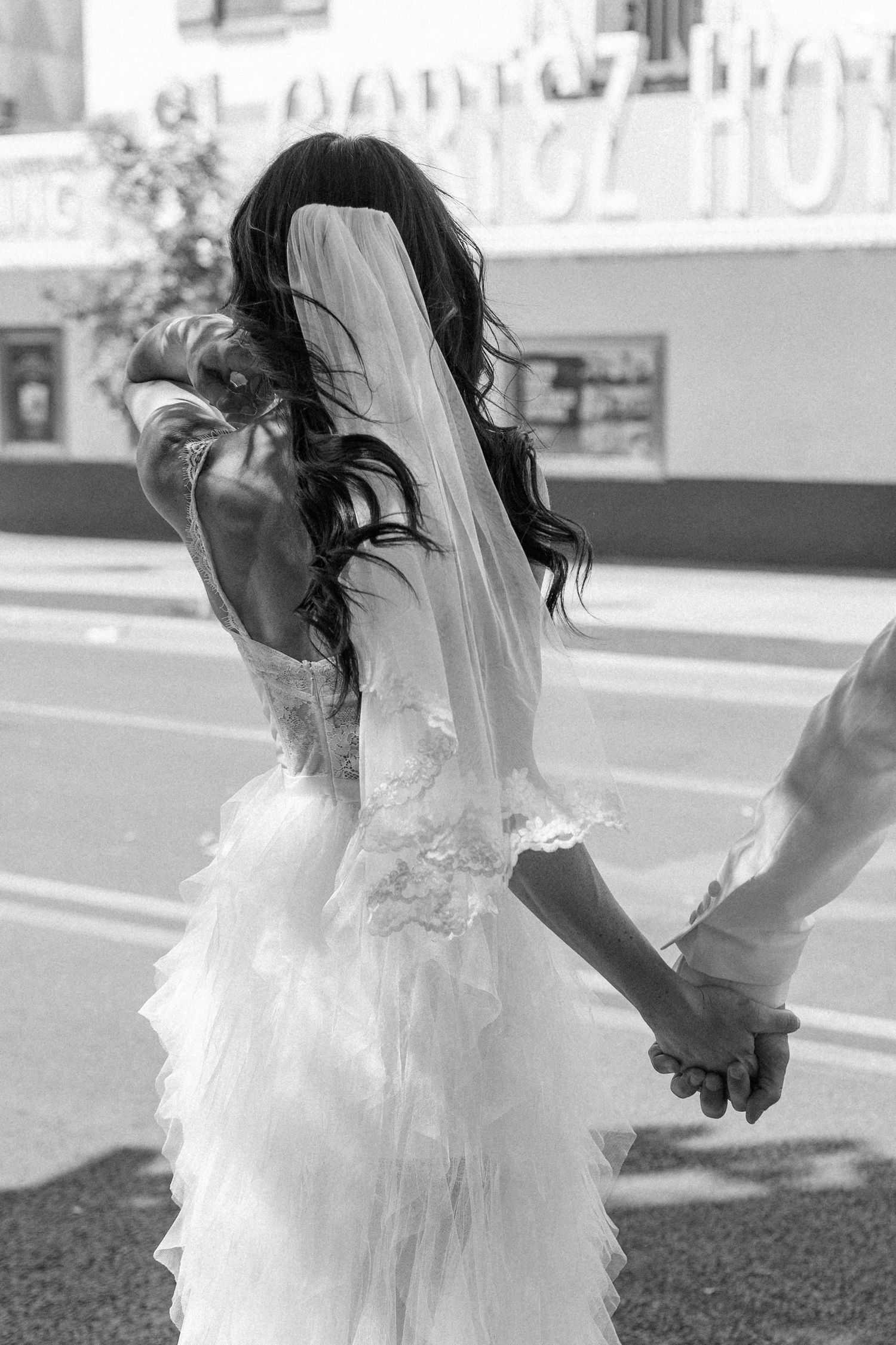A flowing white wedding dress and veil captured in motion against a blurred background.