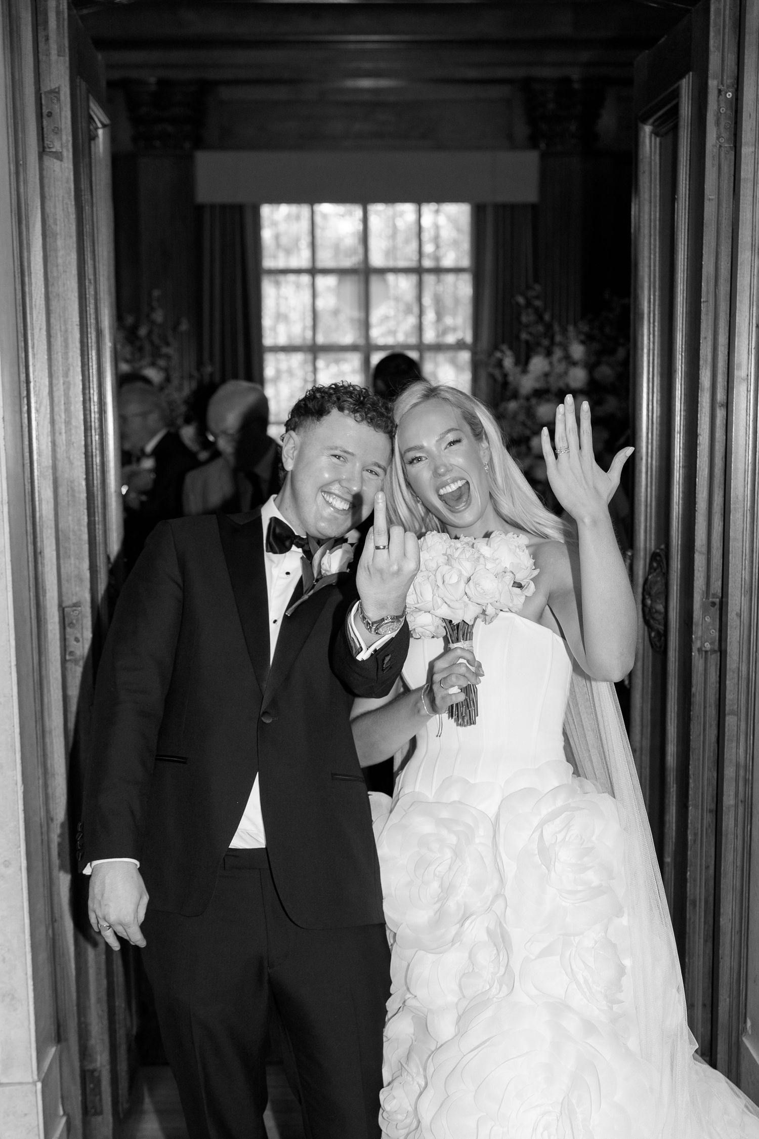 Black and white photo of a joyful bride and groom showing their wedding rings at the altar.