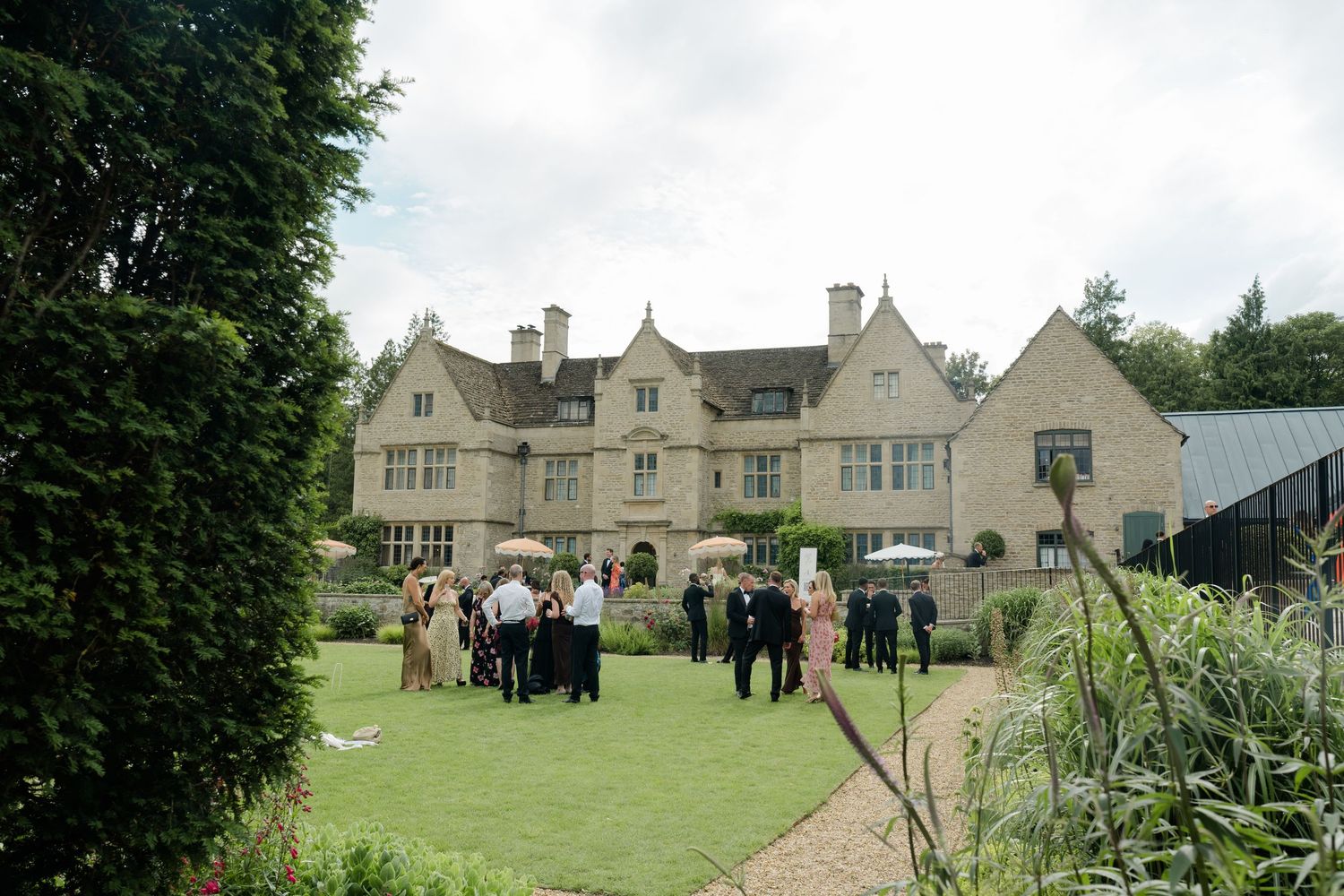 Elegant English manor house wedding venue with guests socializing on lush garden lawn during outdoor reception.