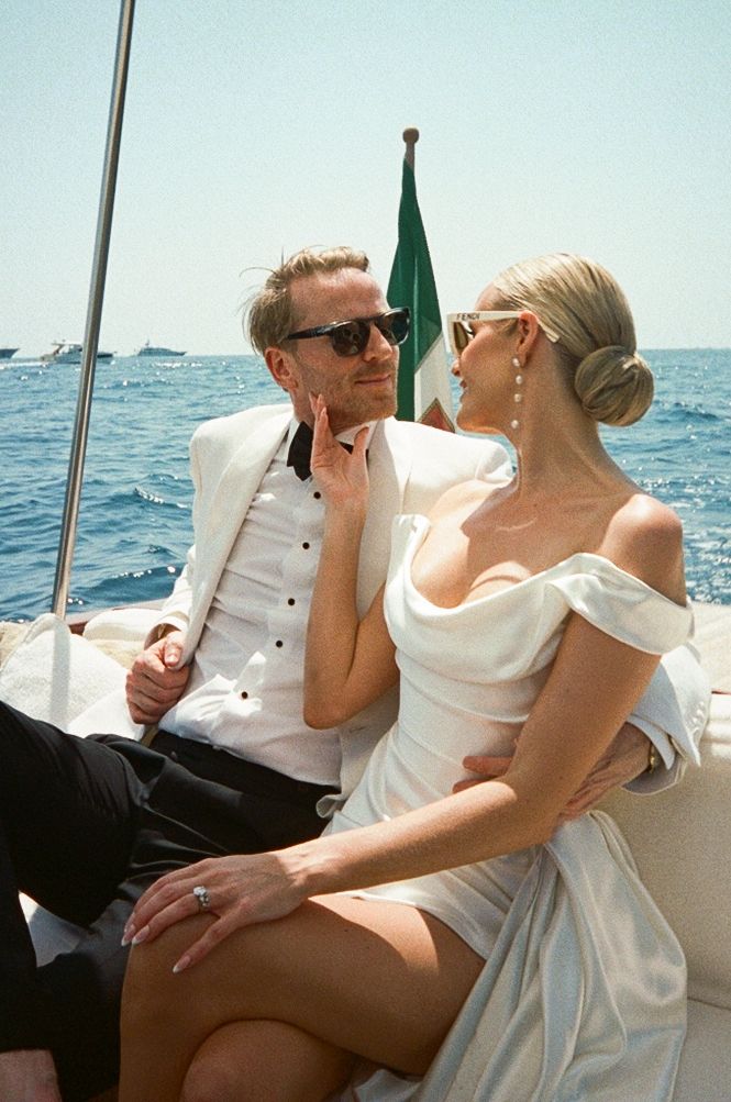 Bride and groom in white wedding outfits sitting on luxury boat on sunny Italian waters.