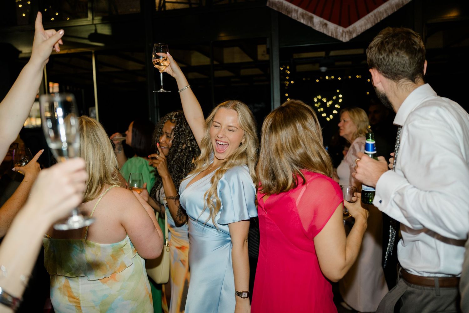 Guests celebrating and dancing at a lively wedding reception party with champagne glasses raised.
