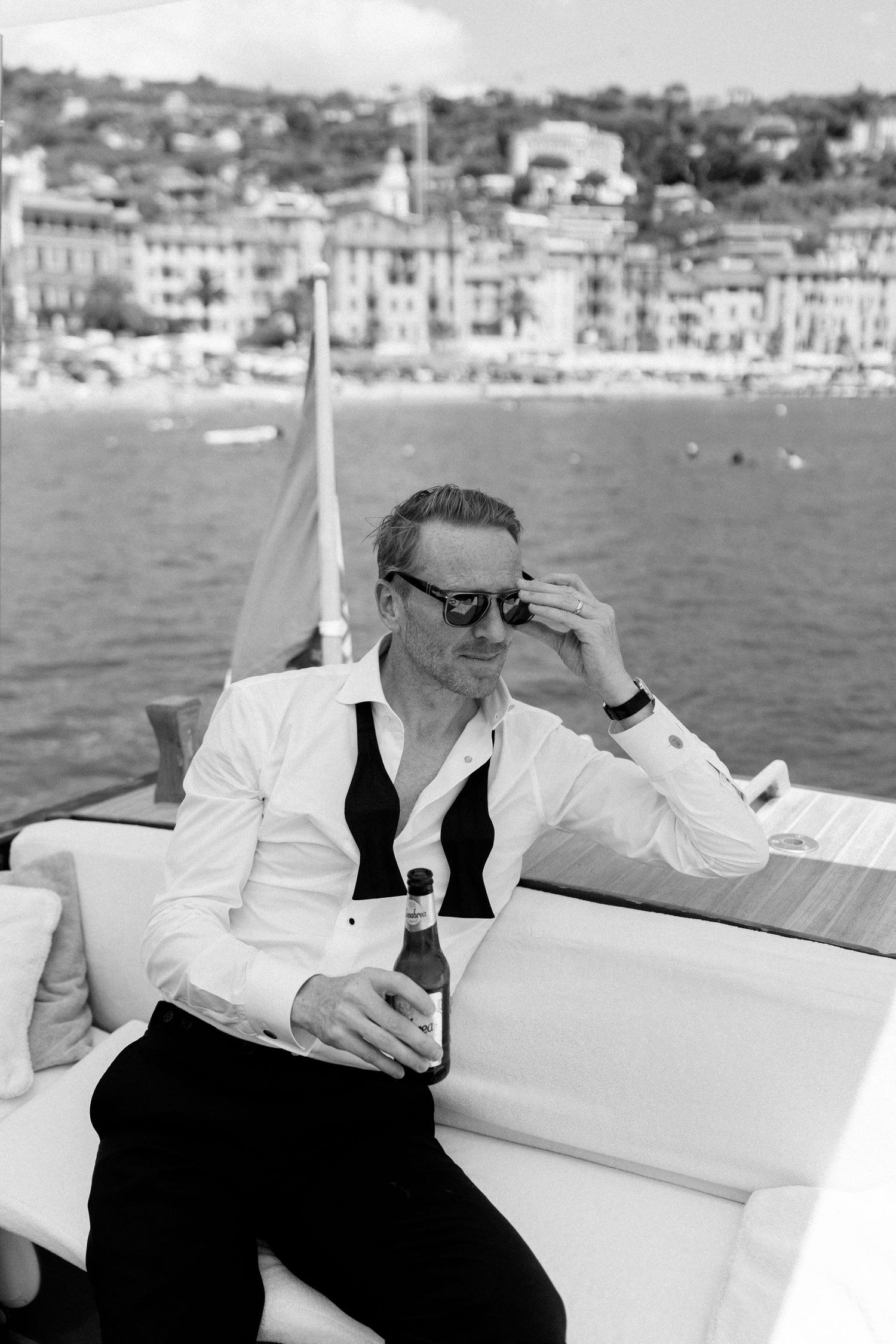 Black and white portrait of stylish groom in white shirt holding beer bottle on a luxury boat in Italy.
