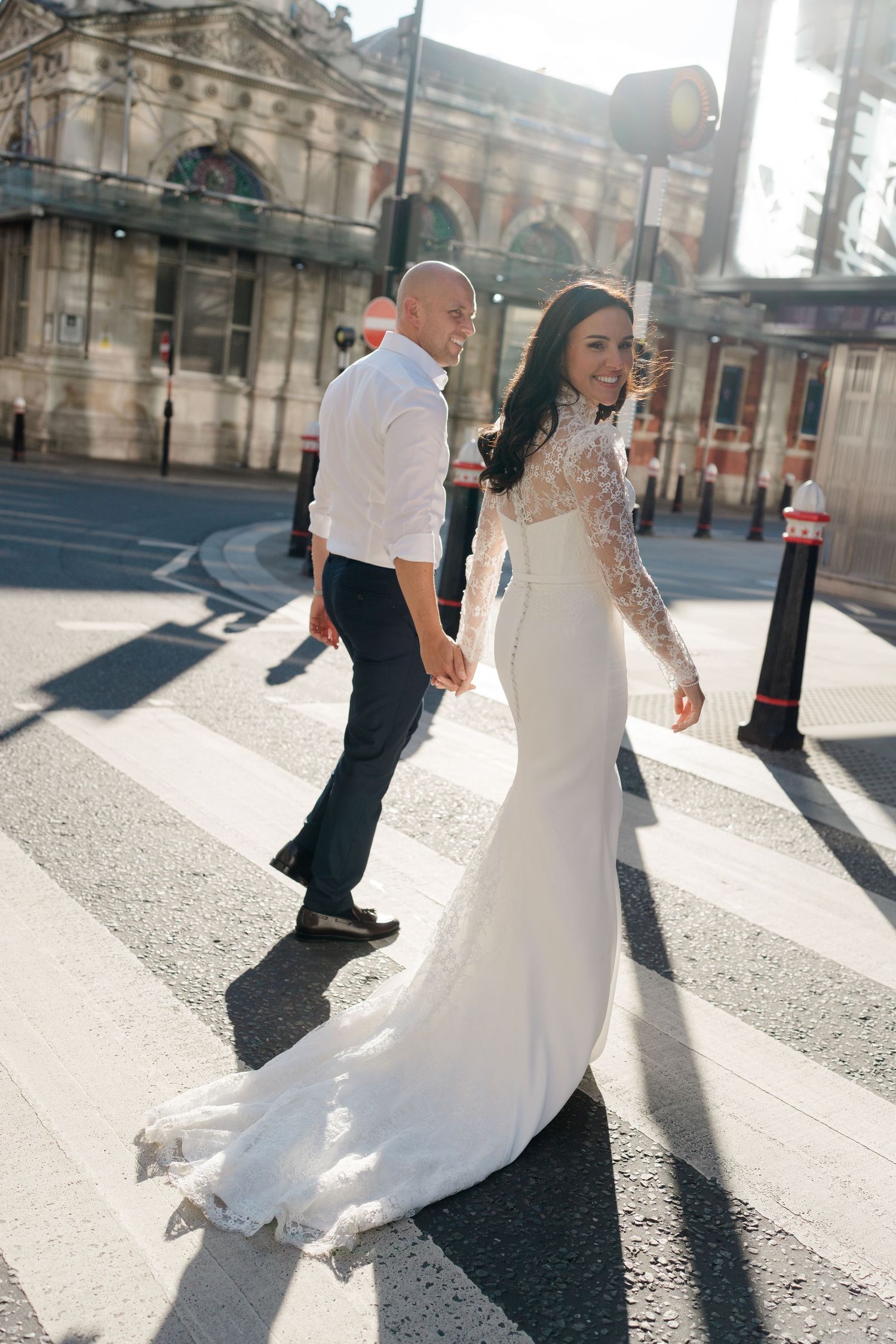 Wedding couple dances in sunlight on city street creating dramatic shadows.