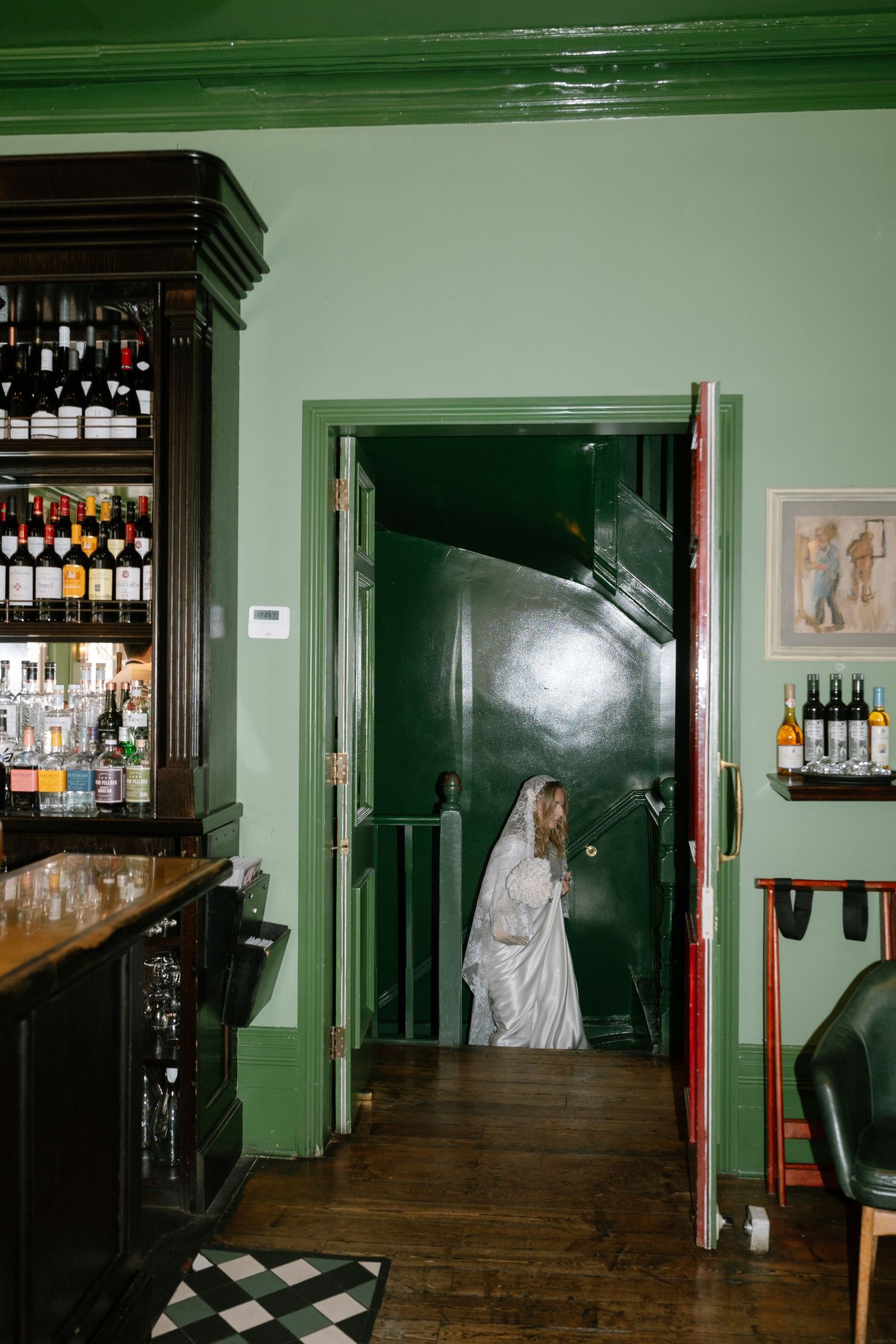 A dimly lit bar interior with dark wood furnishings and green walls shows ghostly figures in white.