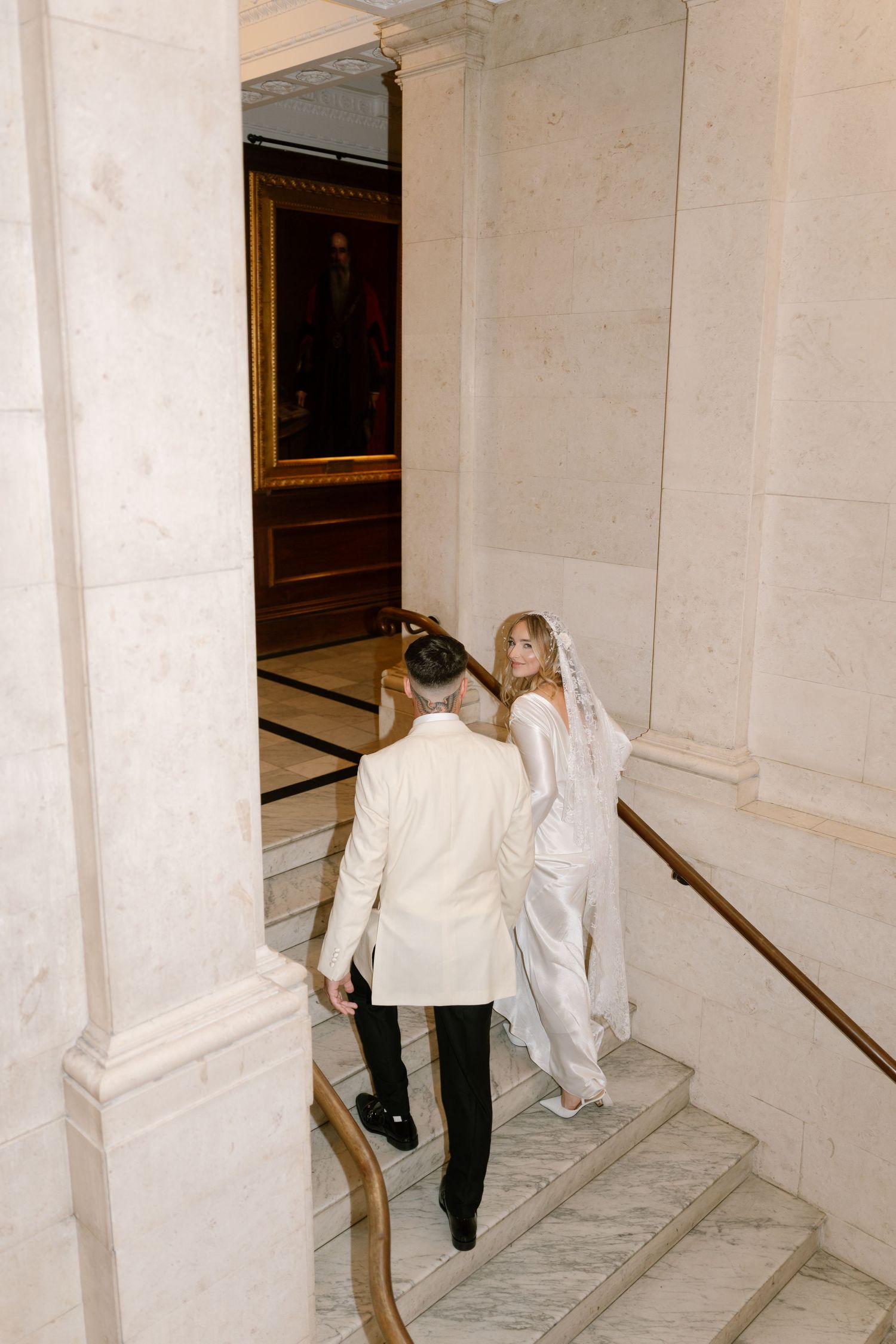 Wedding couple walking through a marble-floored corridor with ornate architectural details.