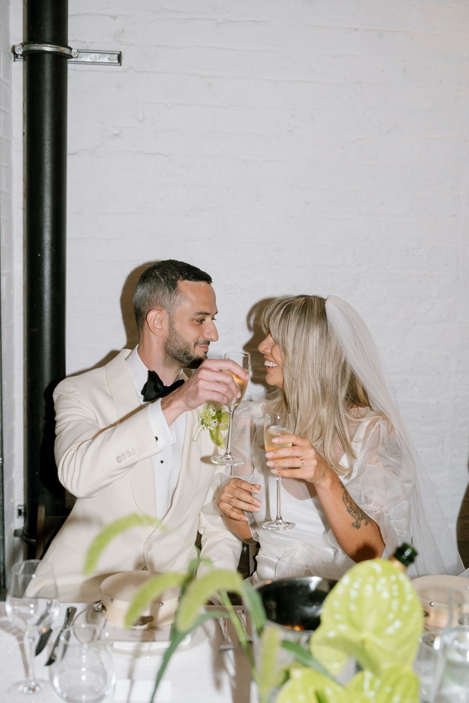 Couple shares intimate moment while toasting with champagne glasses at elegant wedding reception.