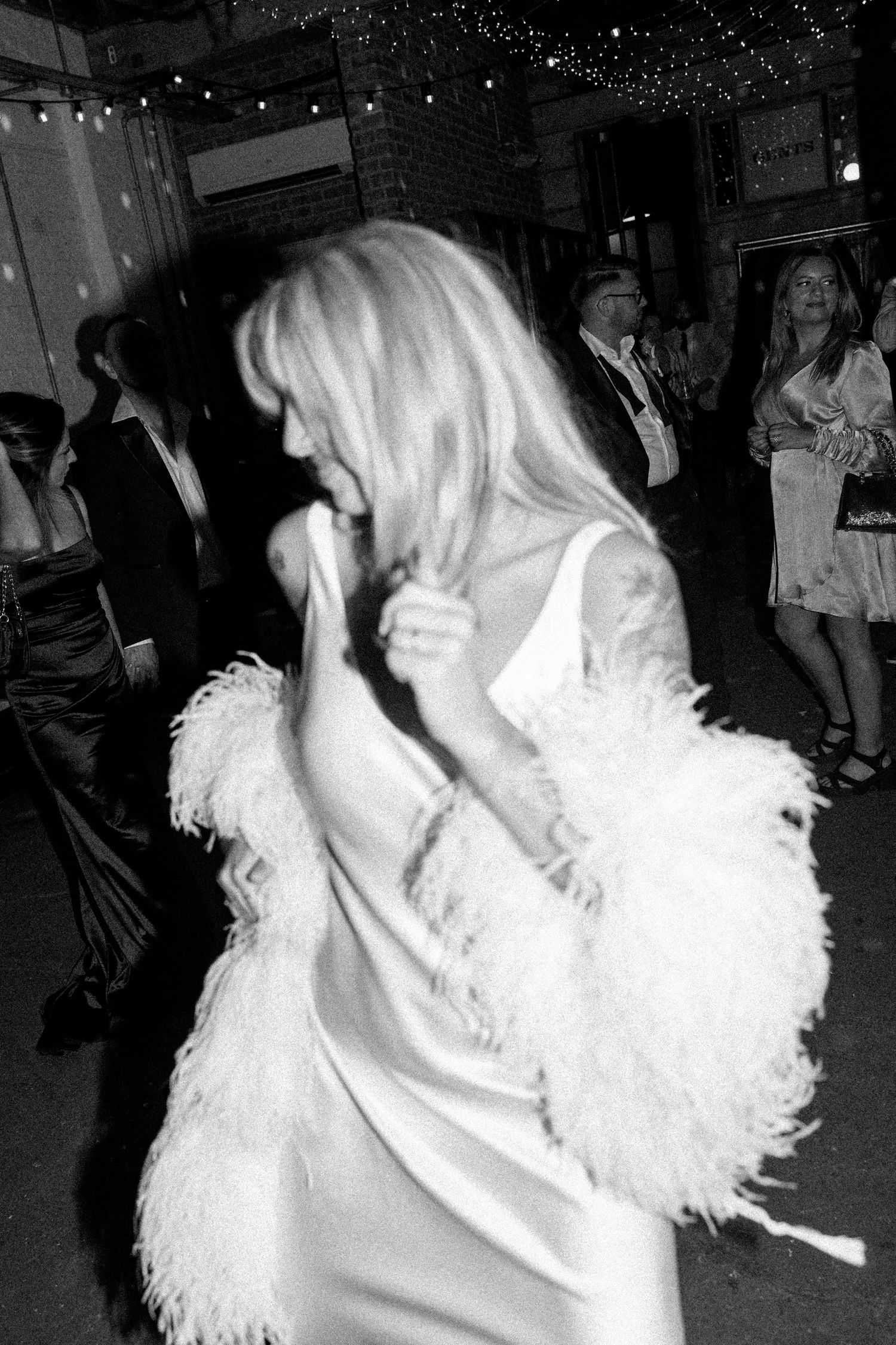 Someone in a white feathered outfit dancing under sparkling lights at a celebration.