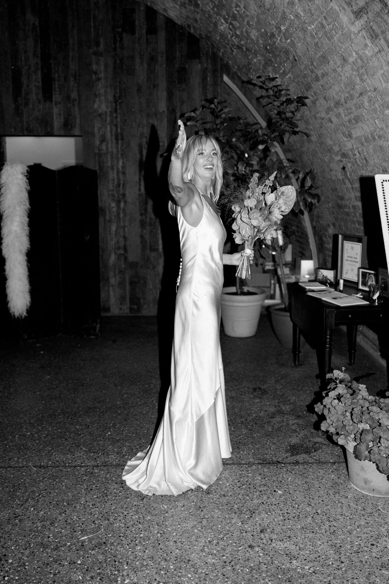 A bride in a silk gown raises her arms in celebration.