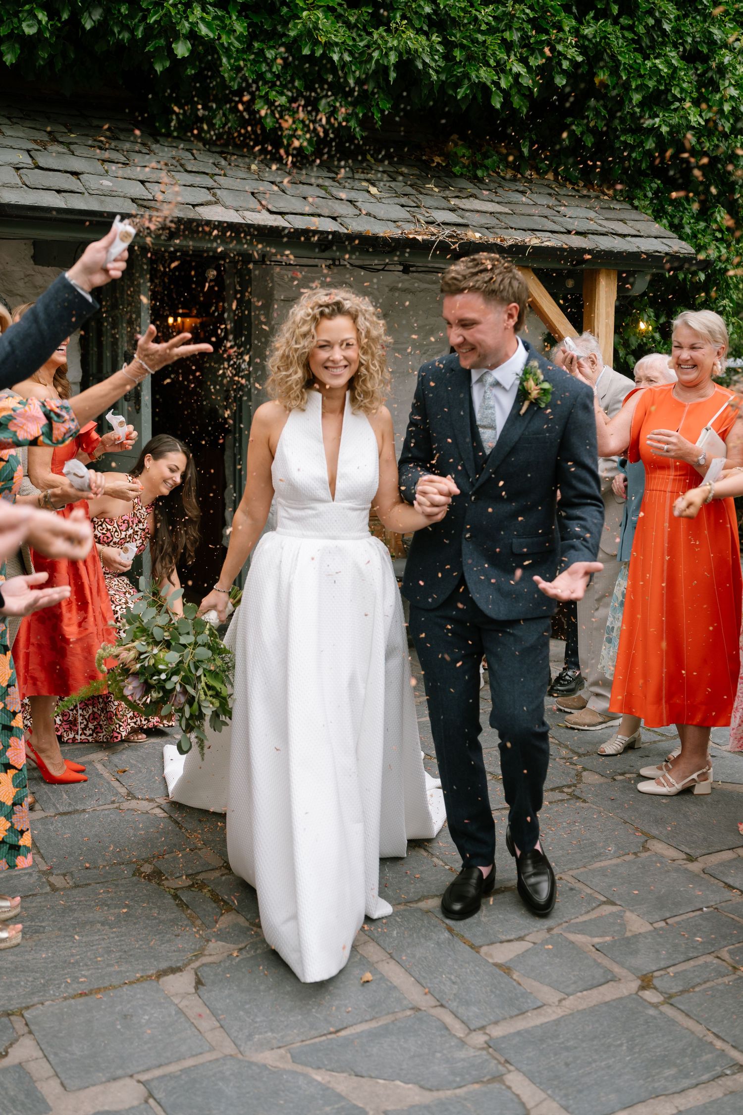 Wedding party celebrates with confetti and dancing on a stone terrace surrounded by greenery.