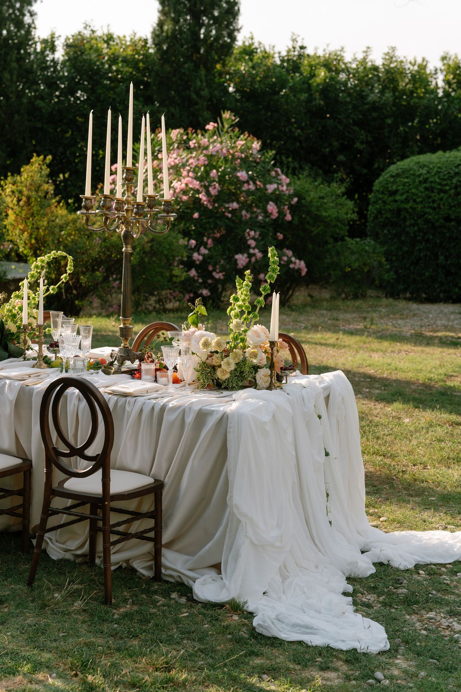 An elegant outdoor wedding reception table setting with white linens and floral decorations.