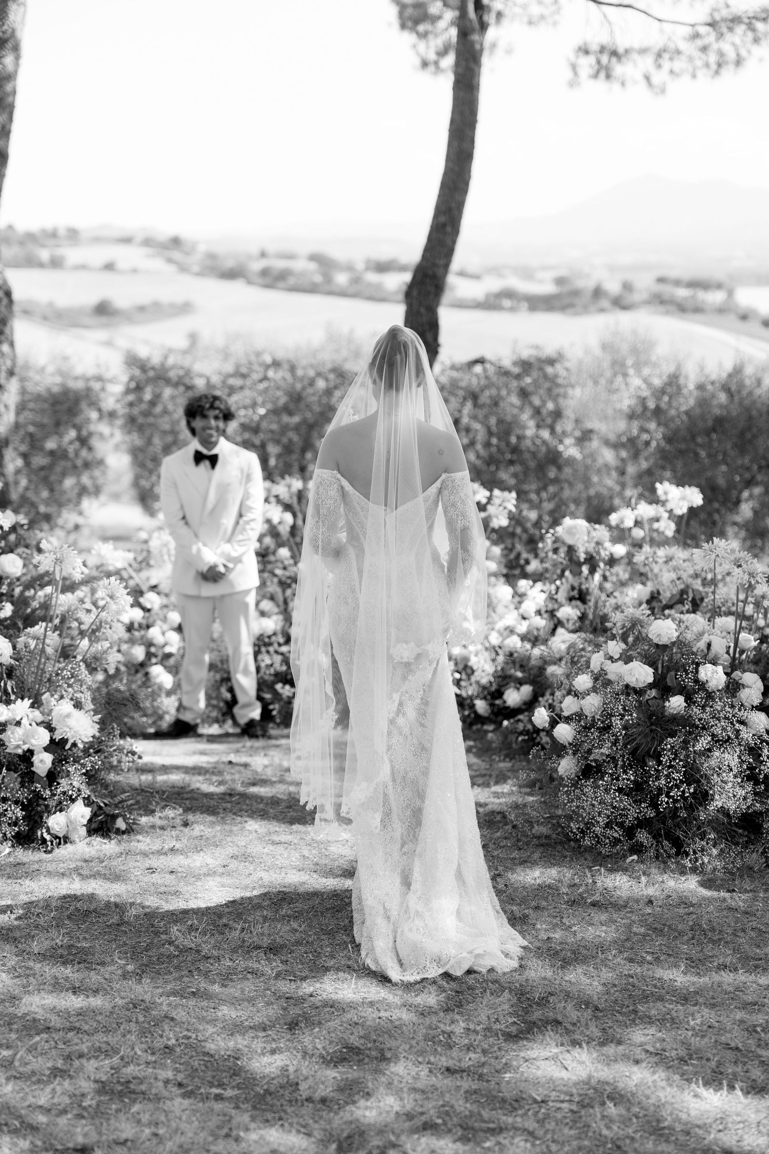 An outdoor garden wedding ceremony with white floral arrangements and flowing veils.
