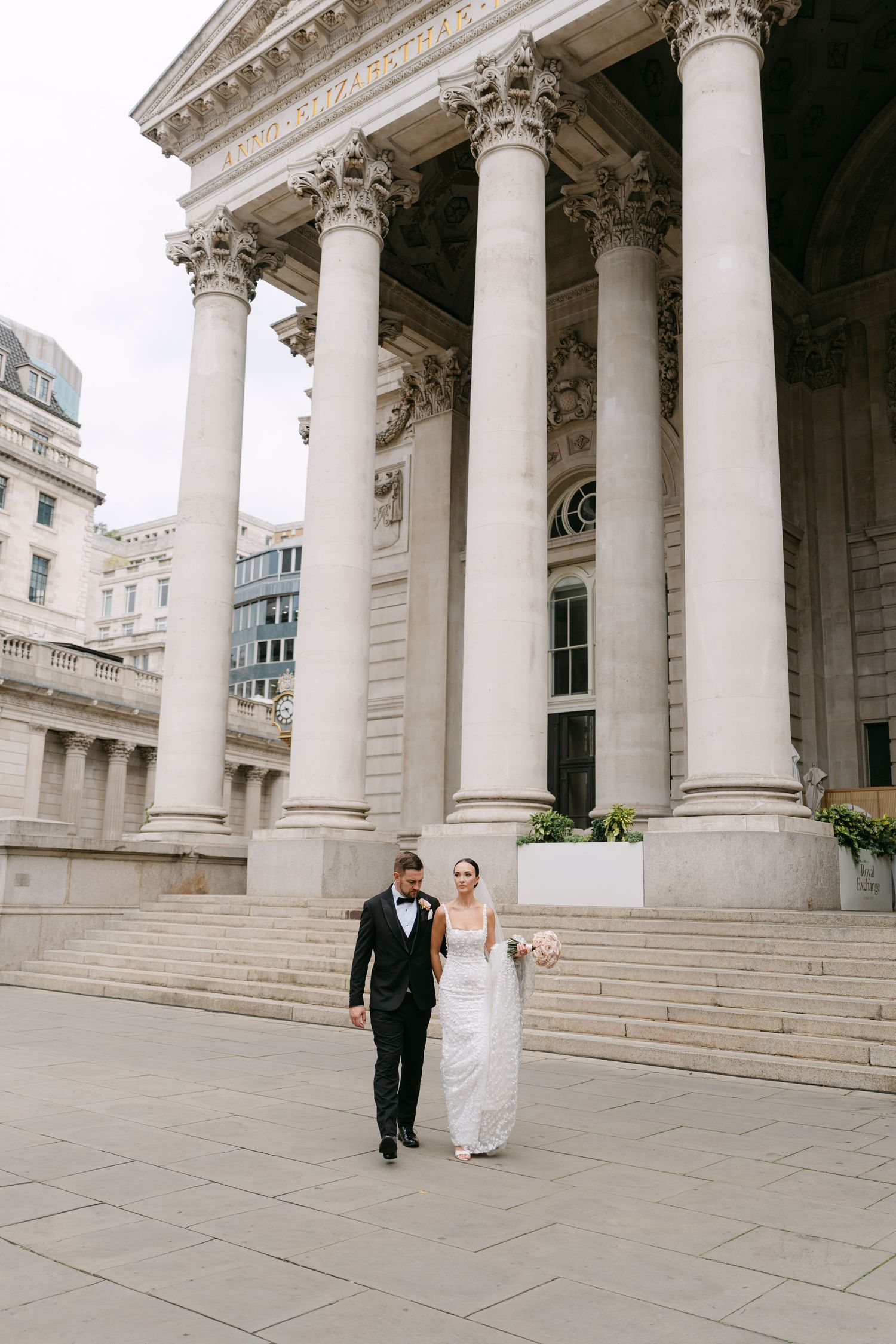 Wedding couple walking along grand classical building with white columns and stone steps.