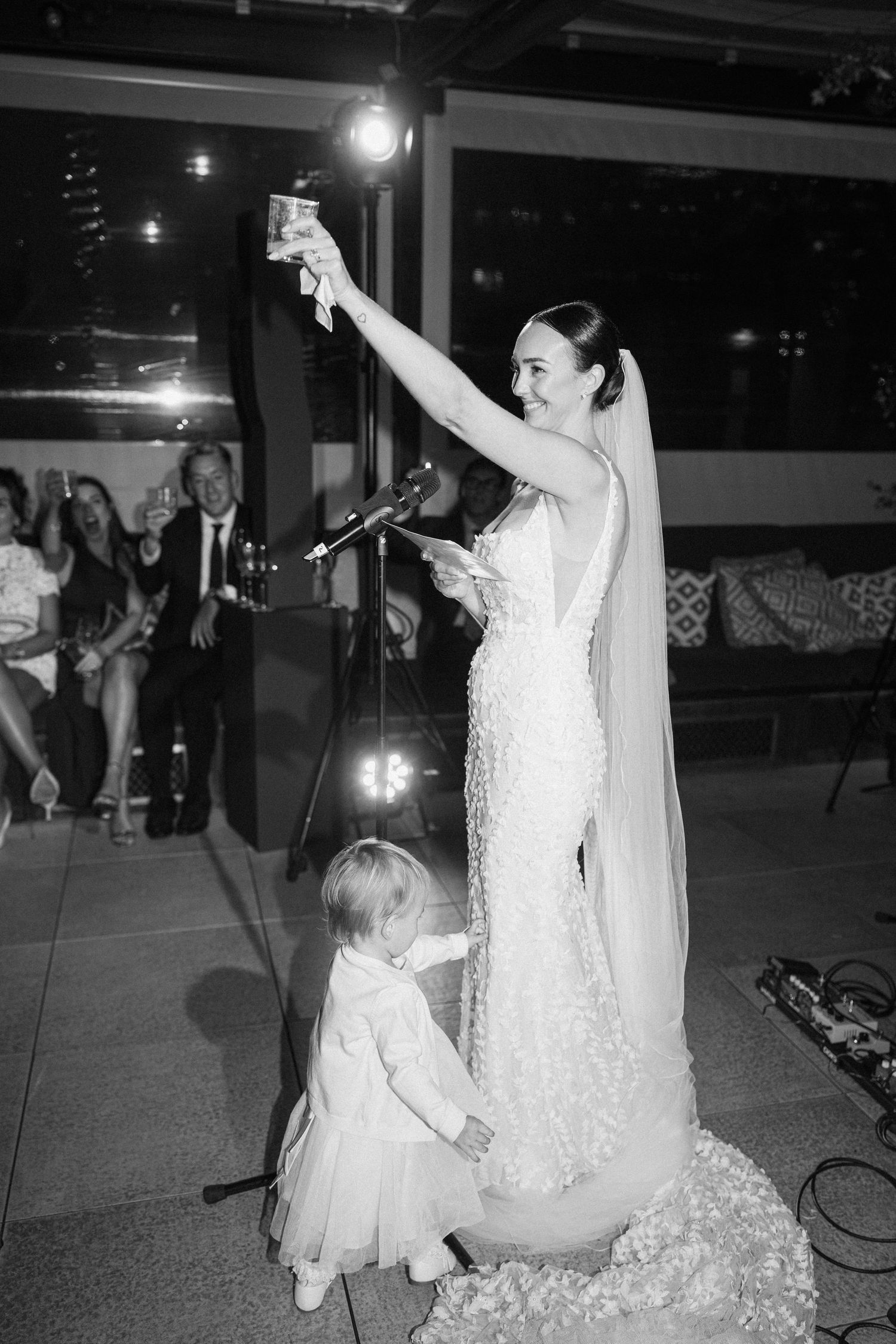 A bride in a white dress dances with a small child during a wedding reception.