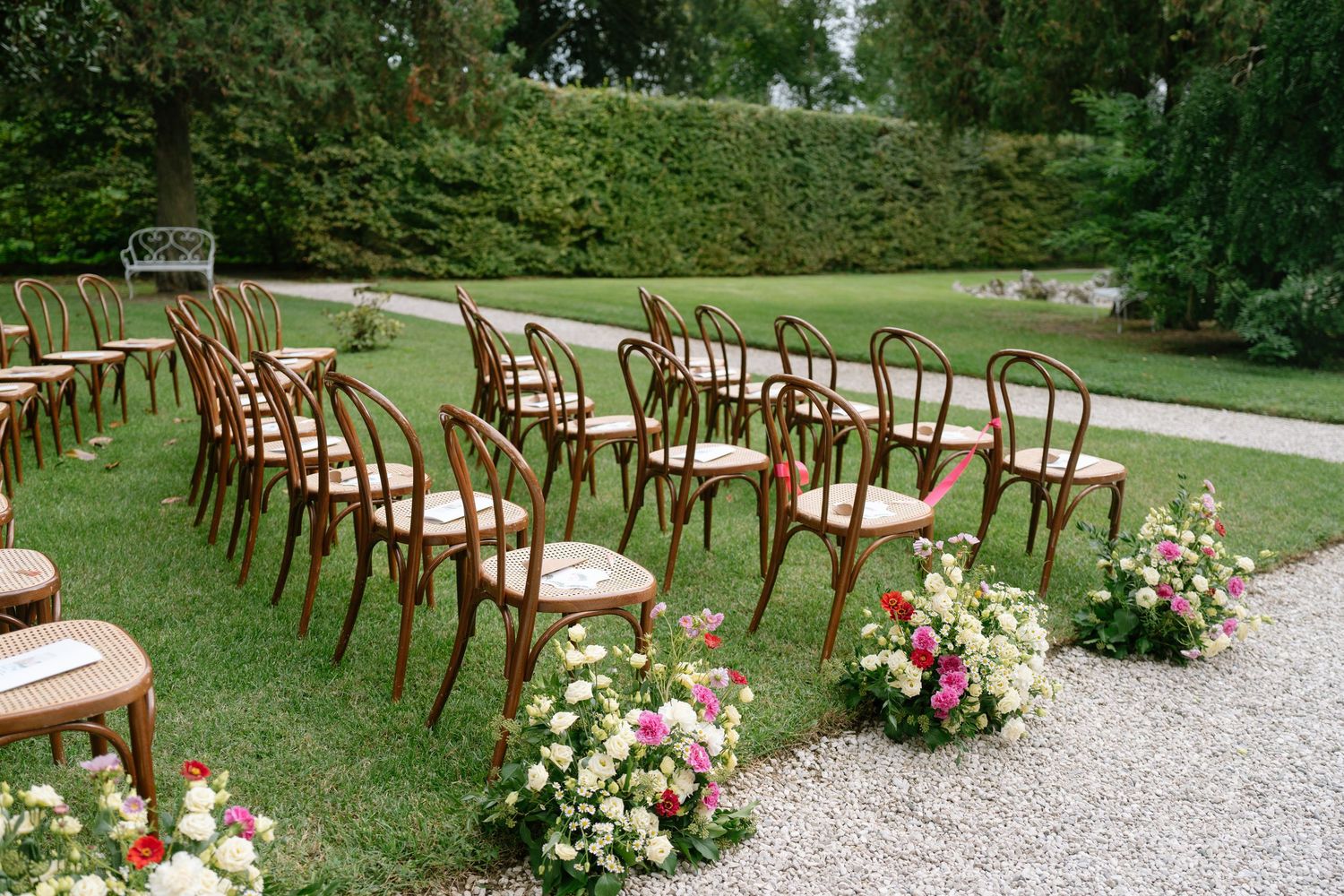 Rows of wooden chairs arranged outdoors on a gravel path for a garden ceremony.