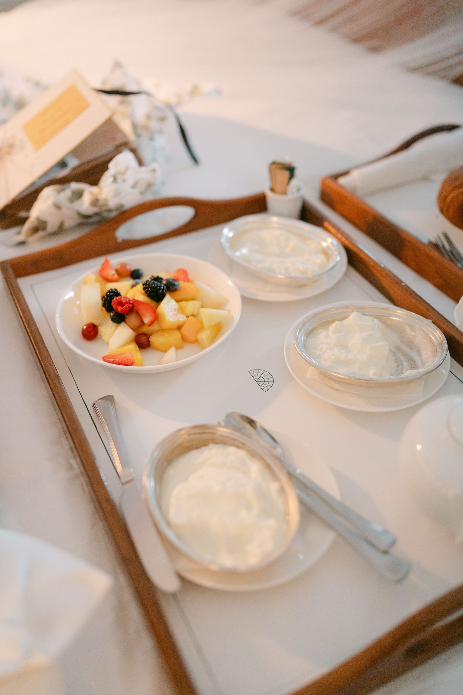 Elegant place settings with fruit and cream desserts served on wooden trays.