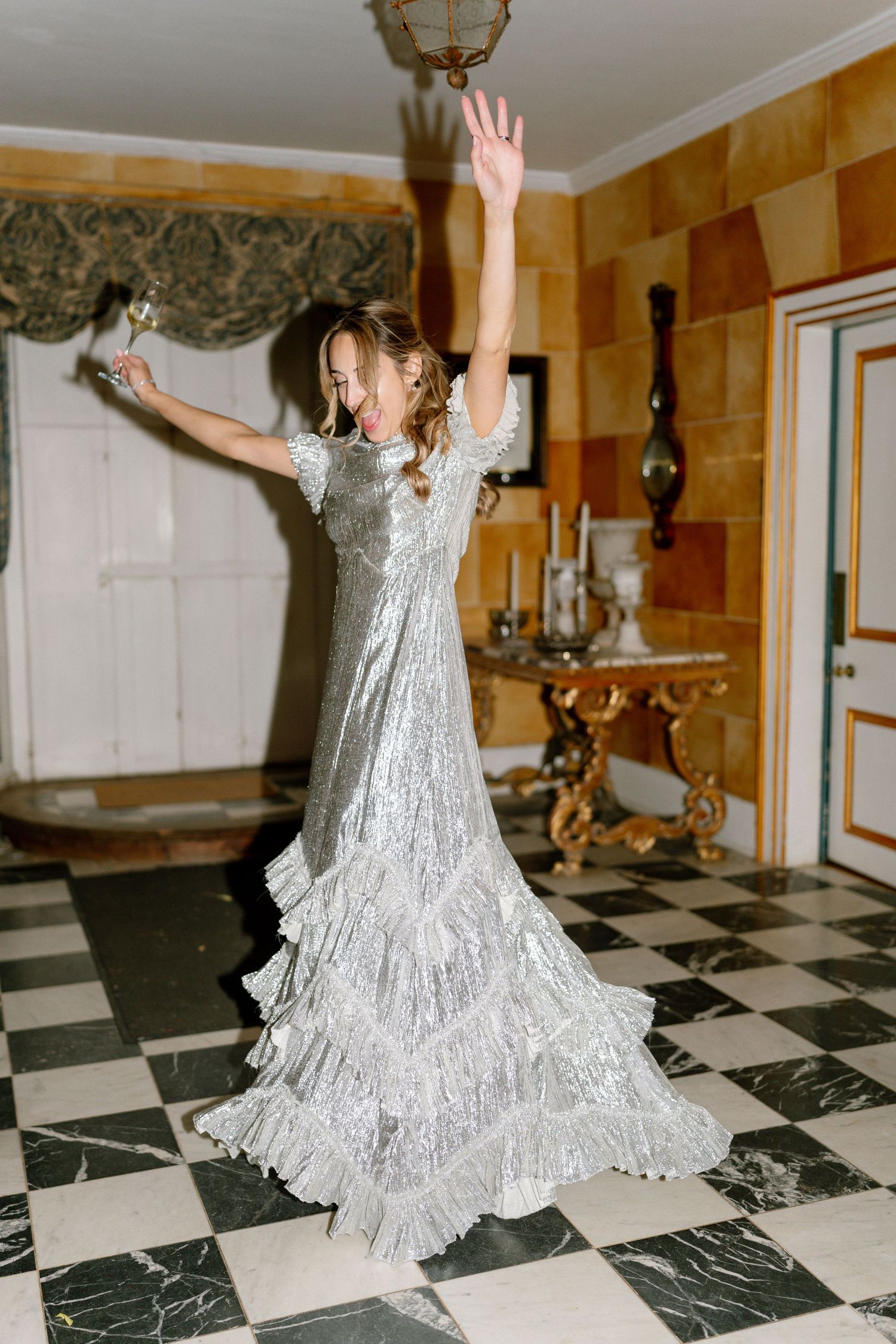 A figure in a flowing silver dress twirls on a black and white checkered floor in an ornate room.