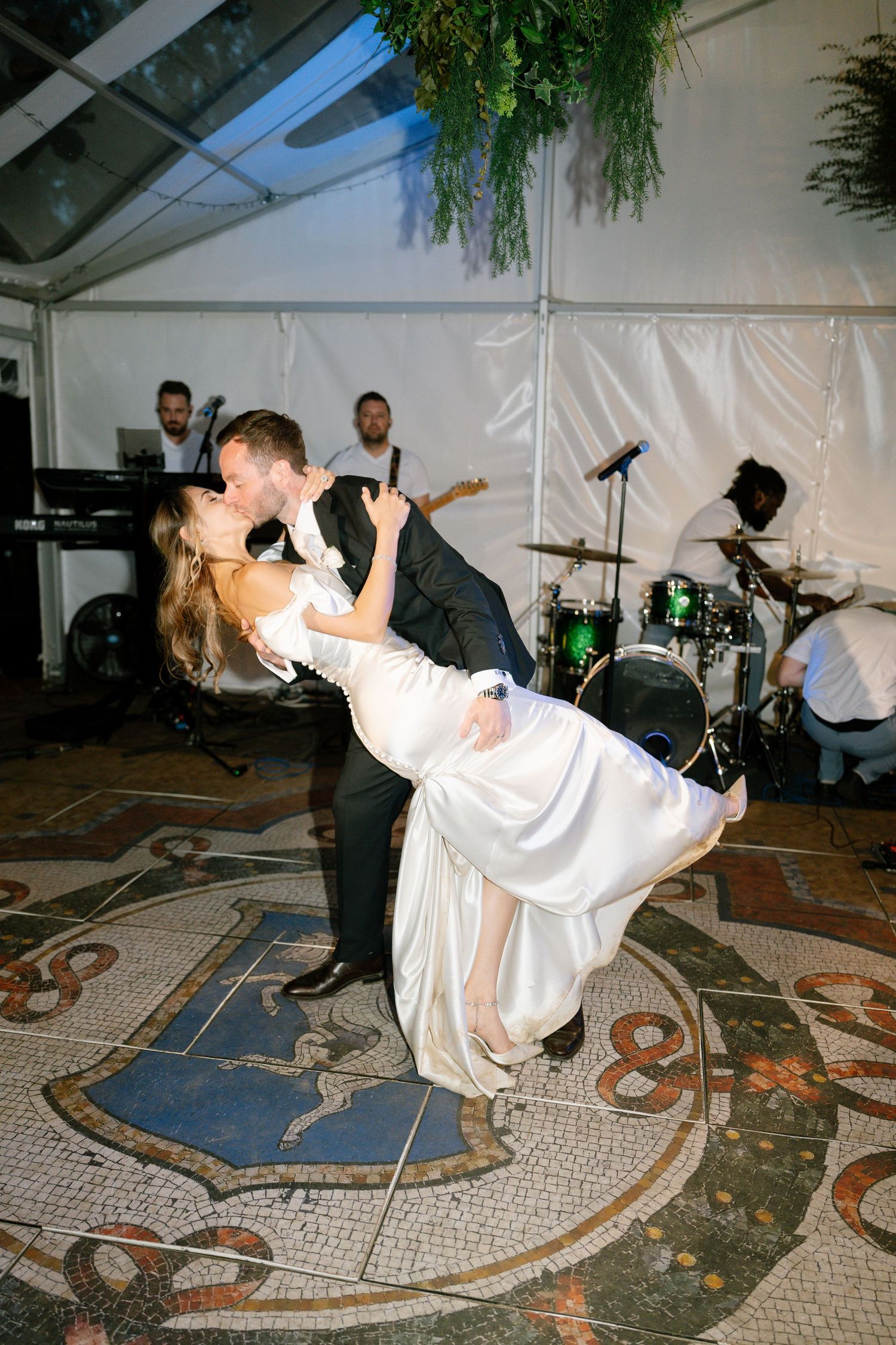 A couple performs a dramatic dip during their wedding dance on a mosaic-patterned floor.