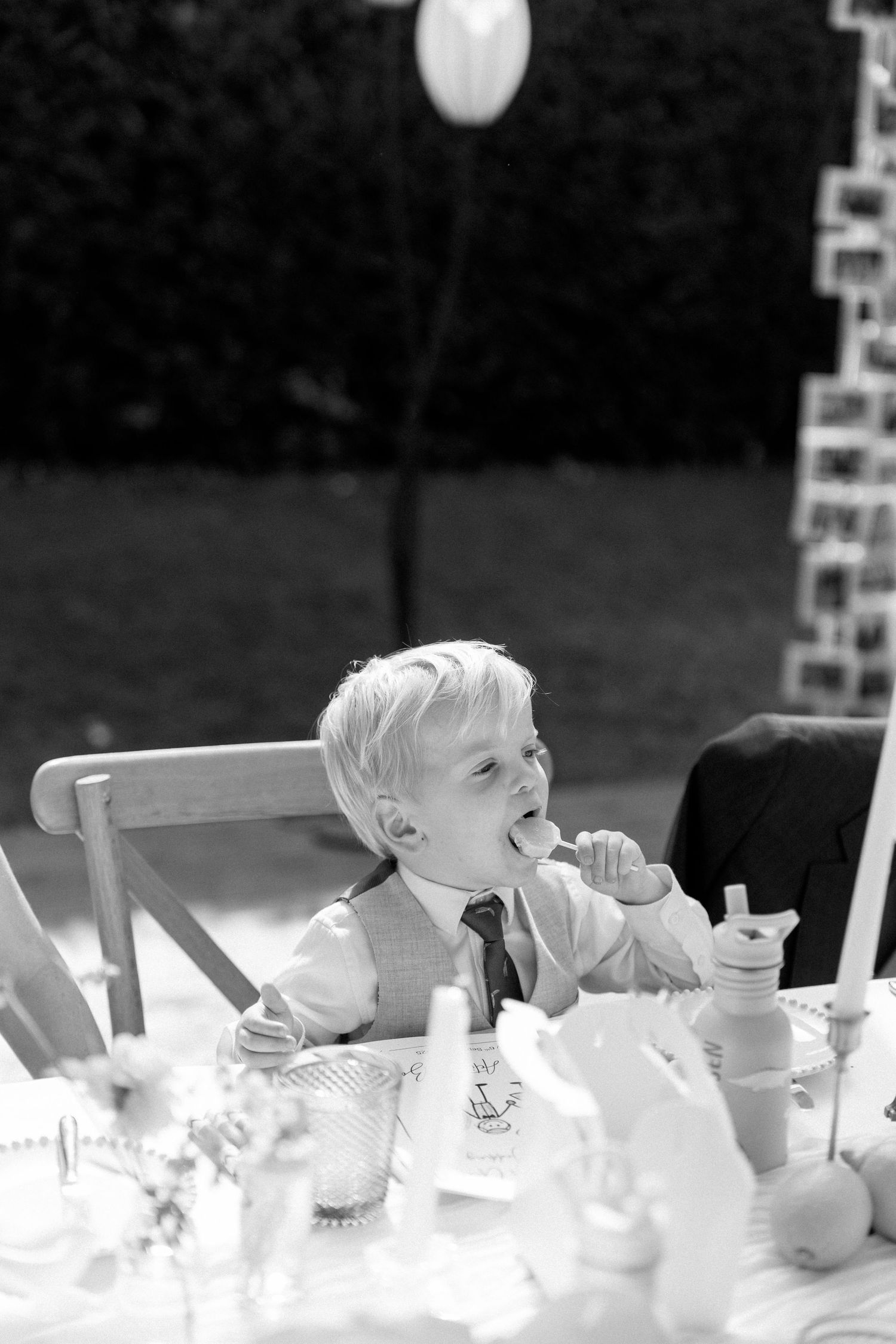 Young boy in formal attire enjoying dessert at an elegant outdoor table setting.