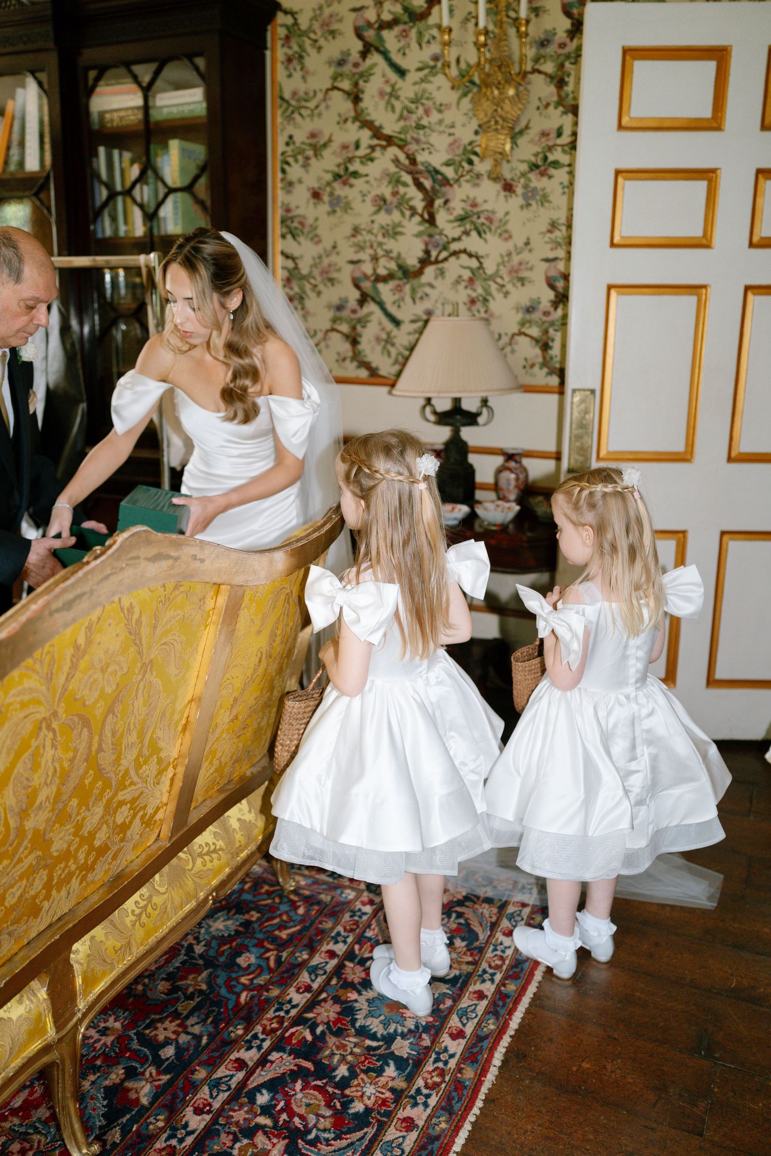 Young attendants in white dresses twirl and play on an ornate rug.