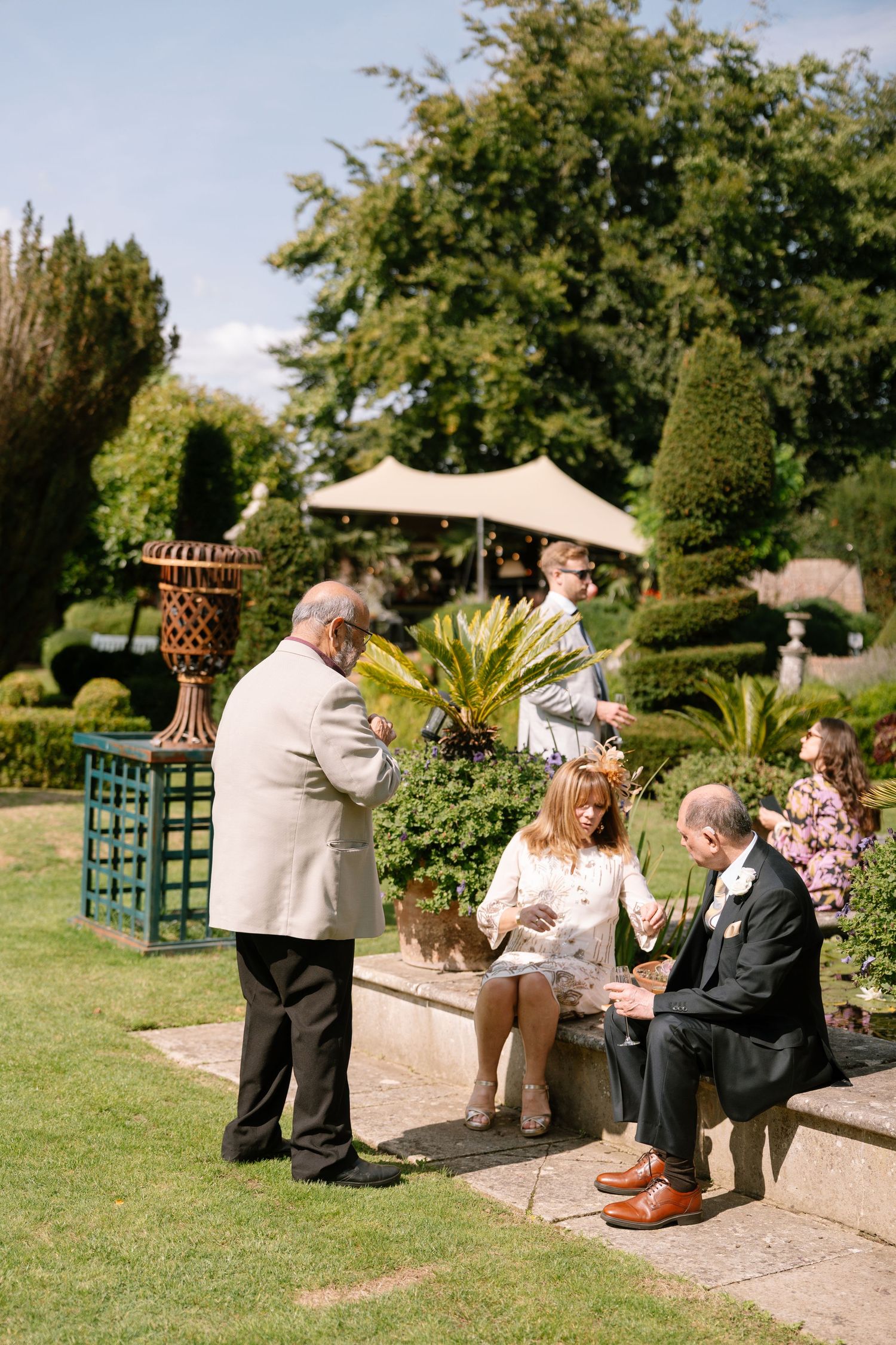 Guests enjoy refreshments on a stone patio surrounded by lush garden landscaping.